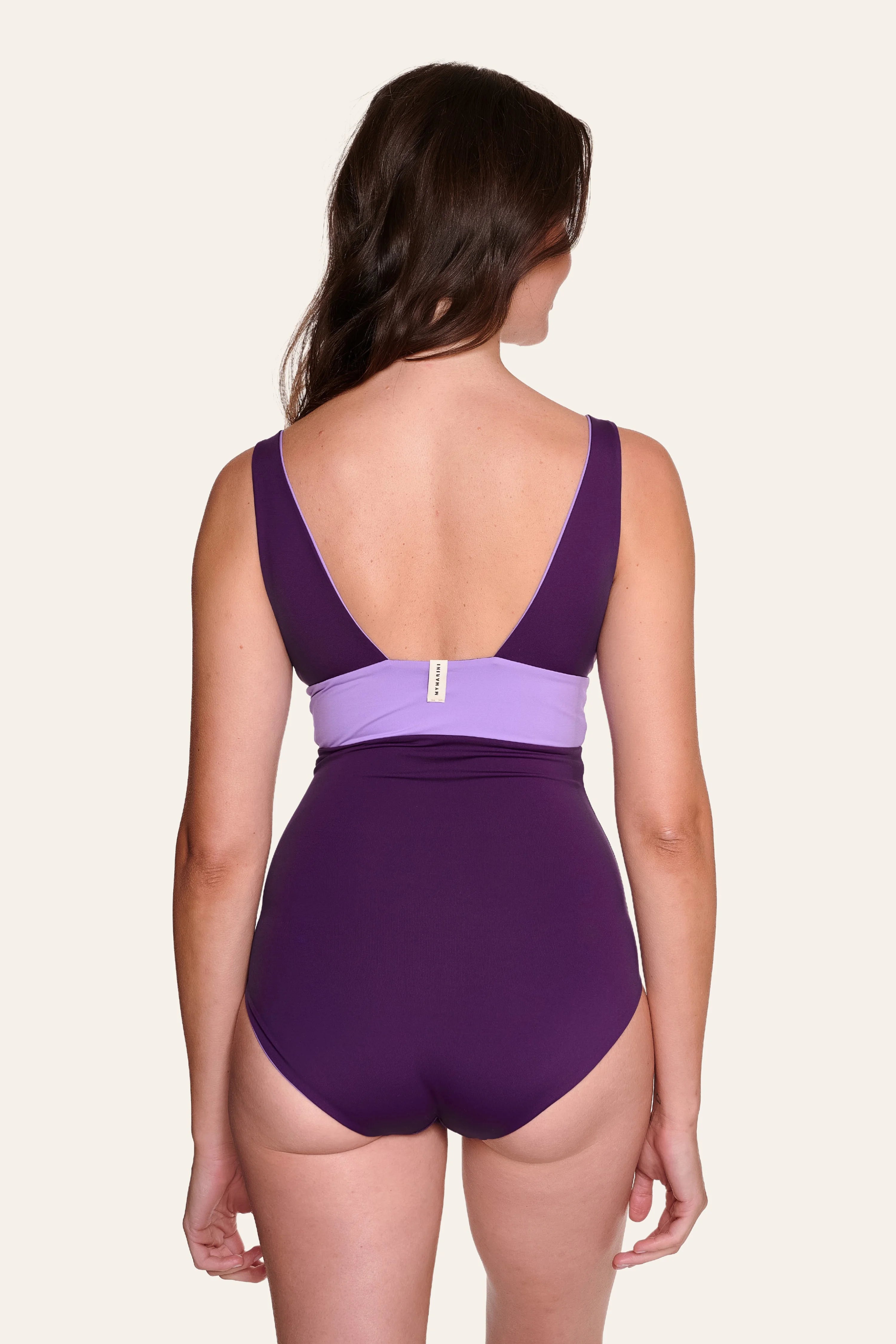 Frau in lila MYMARINI Badeanzug mit tiefem Rückenausschnitt und breiten Trägern, von hinten gezeigt.#color_lavender-plum