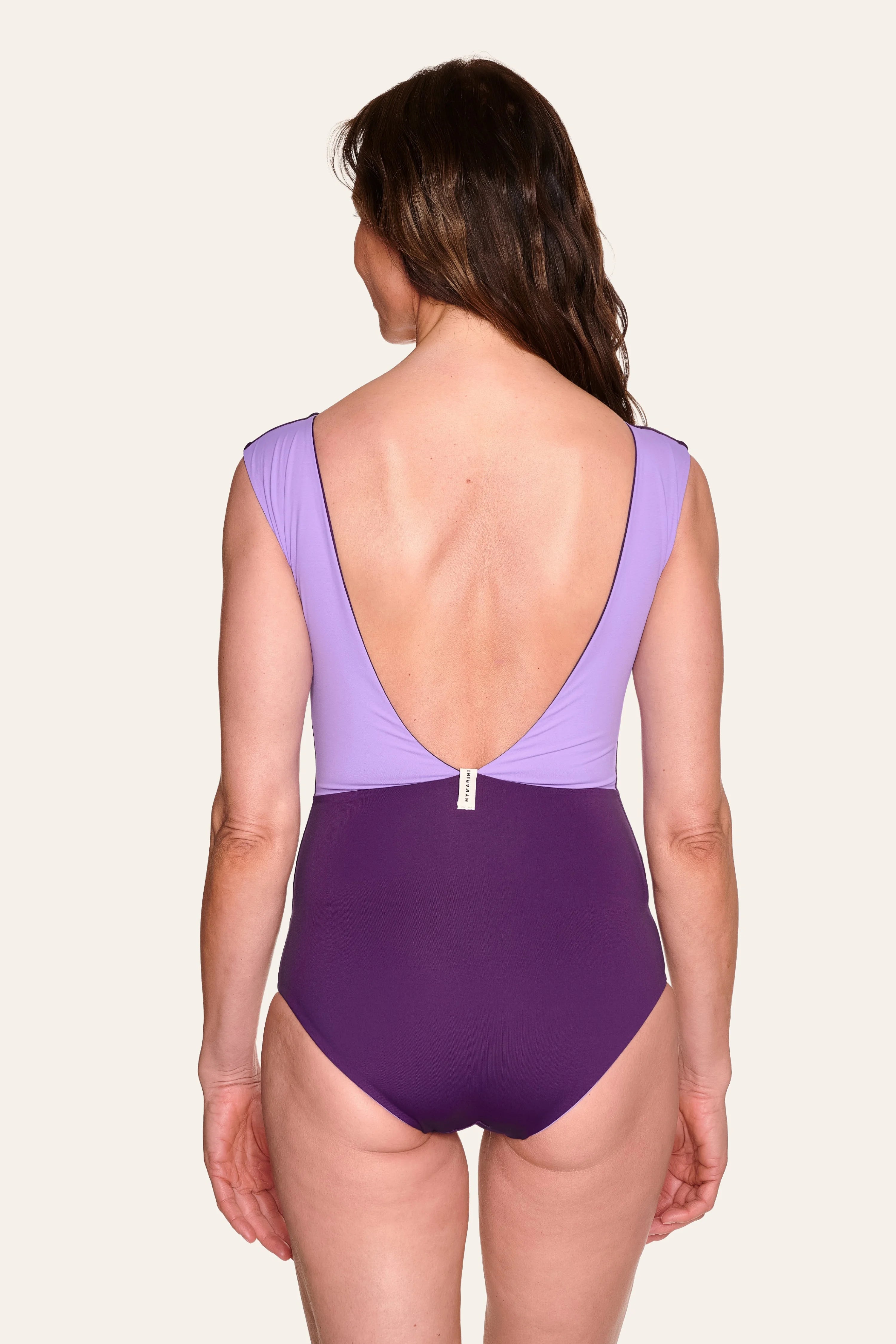 Frau in lila MYMARINI Badeanzug mit tiefem Rückenausschnitt und breiten Trägern, von hinten gesehen.#color_lavender-plum