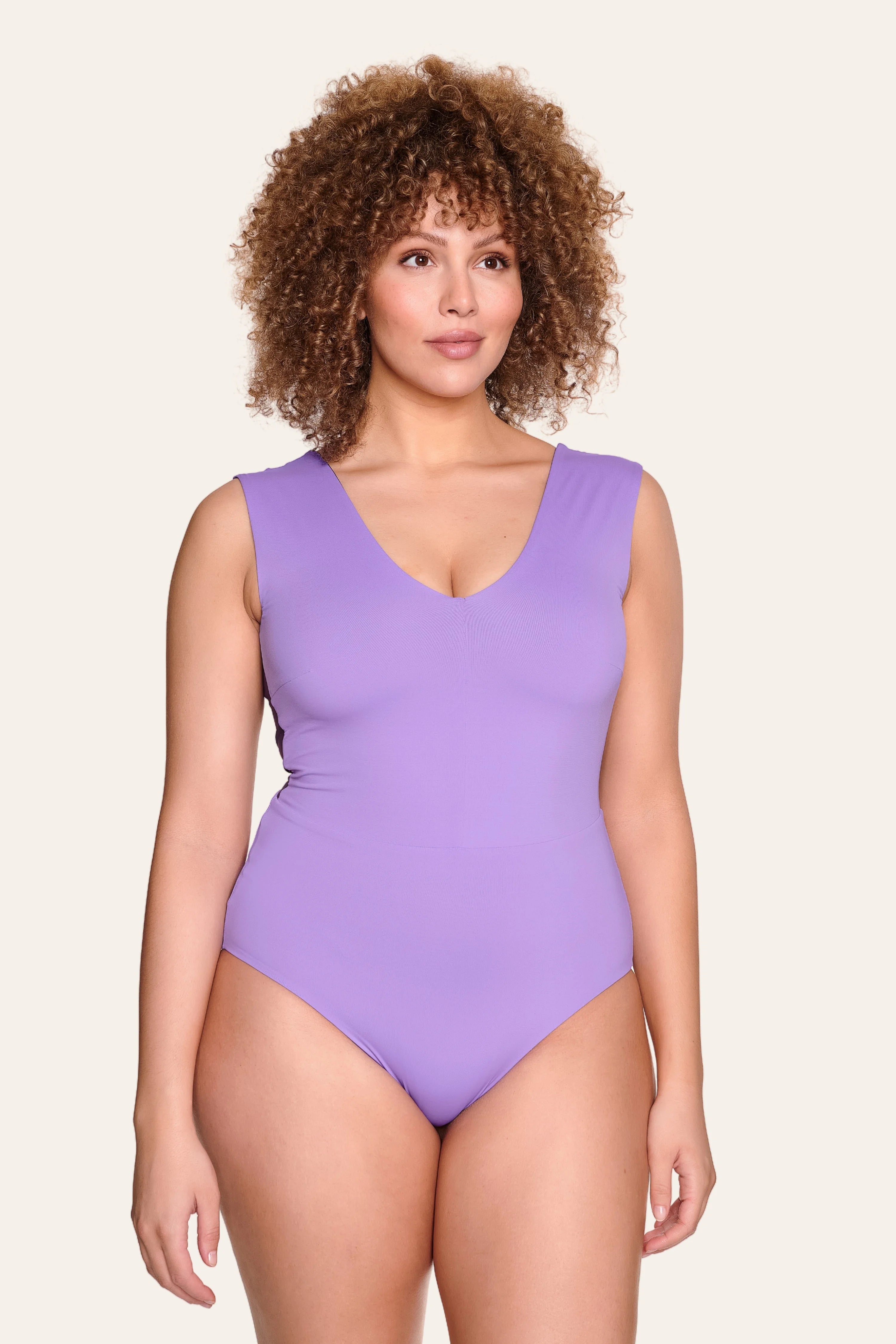 Frau trägt lila MYMARINI Badeanzug mit V-Ausschnitt und hohem Beinausschnitt vor hellem Hintergrund.#color_lavender-plum
