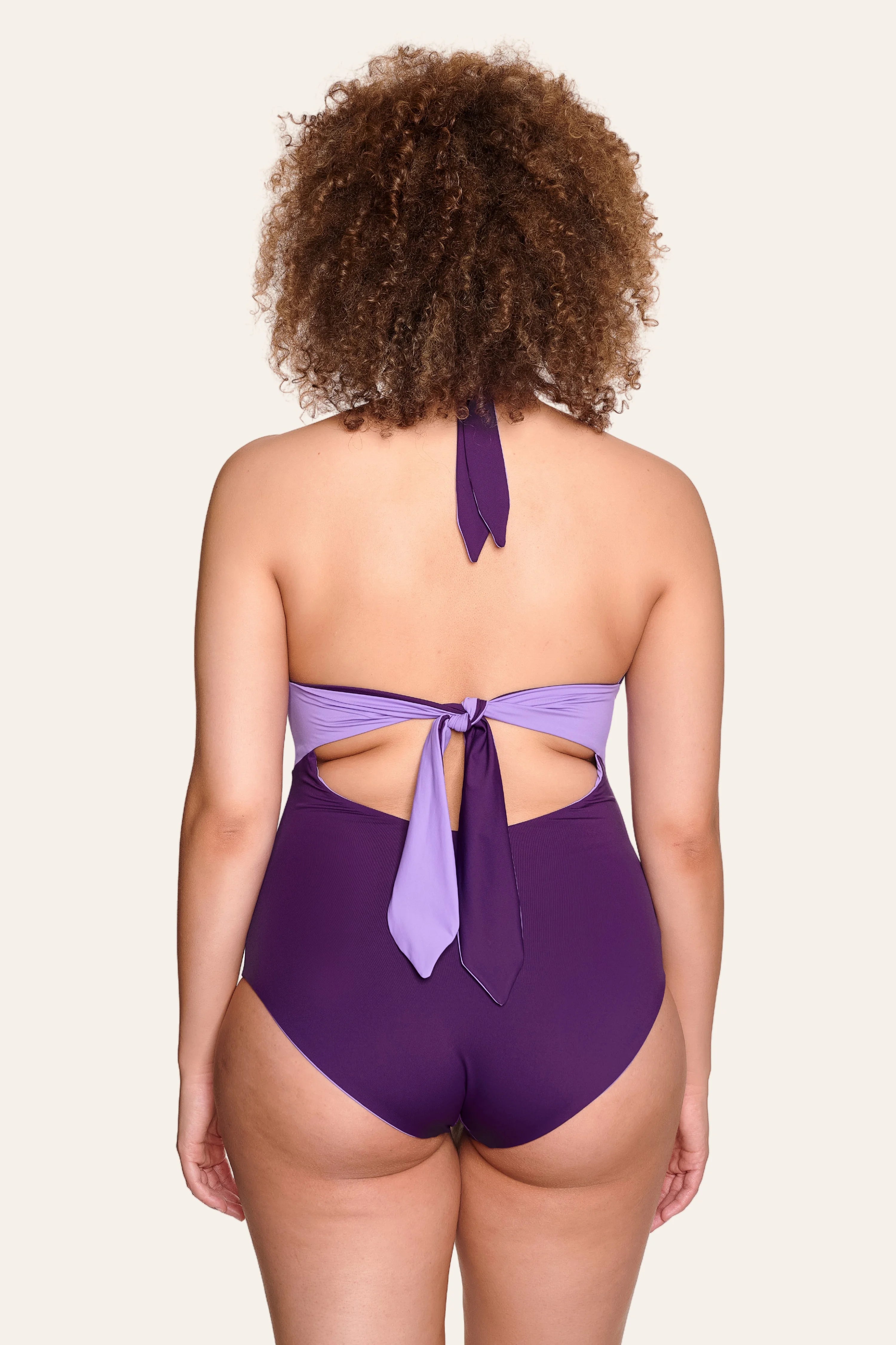 Rückansicht eines lila MYMARINI Neckholder-One-Pieces mit hohem Beinausschnitt und Schleifendetail am Rücken.#color_lavender-plum