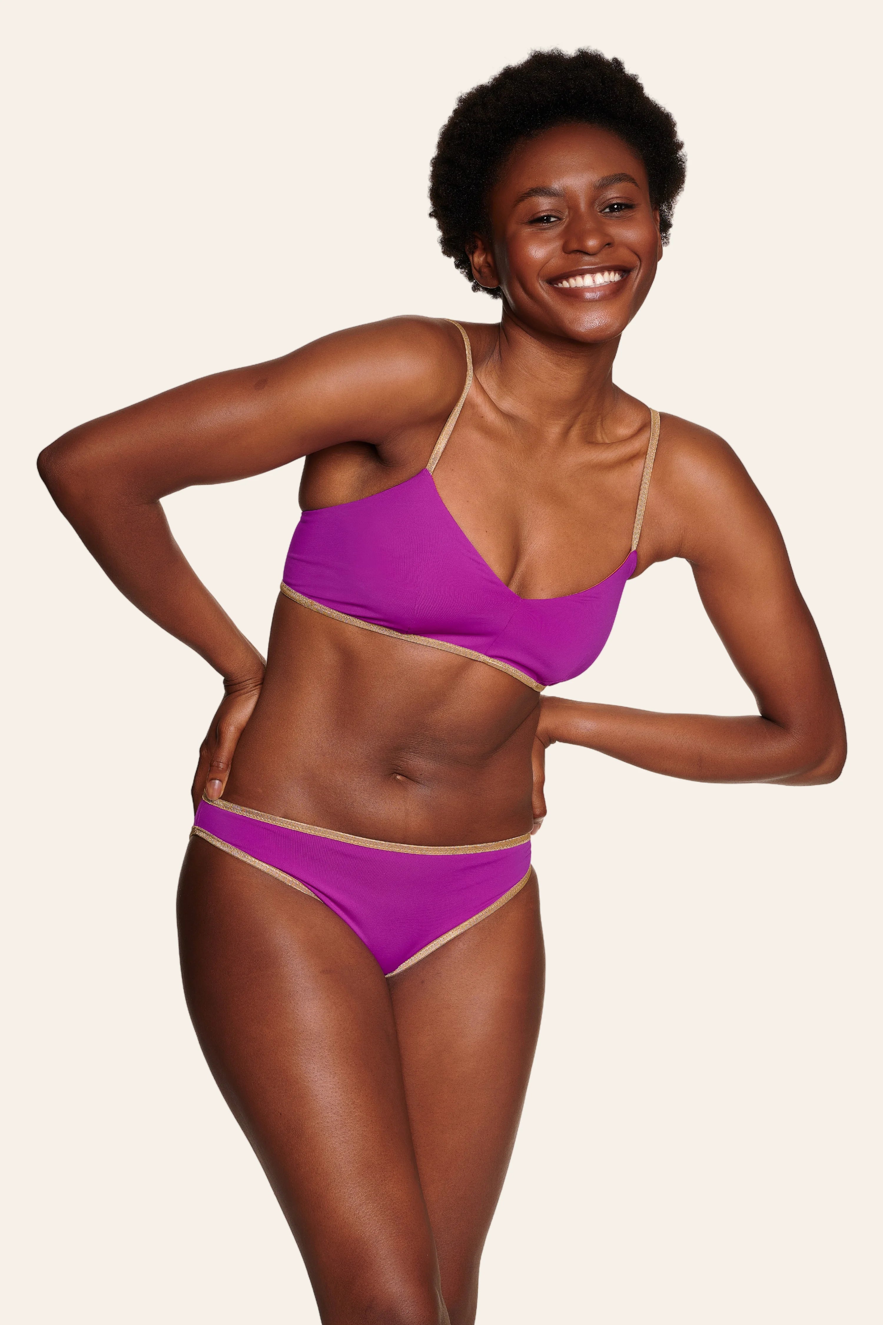 Lächelnde Person trägt MYMARINI Bikinitop mit Spaghettiträgern und Bikinihose in Lila.#color_papaya-cassis