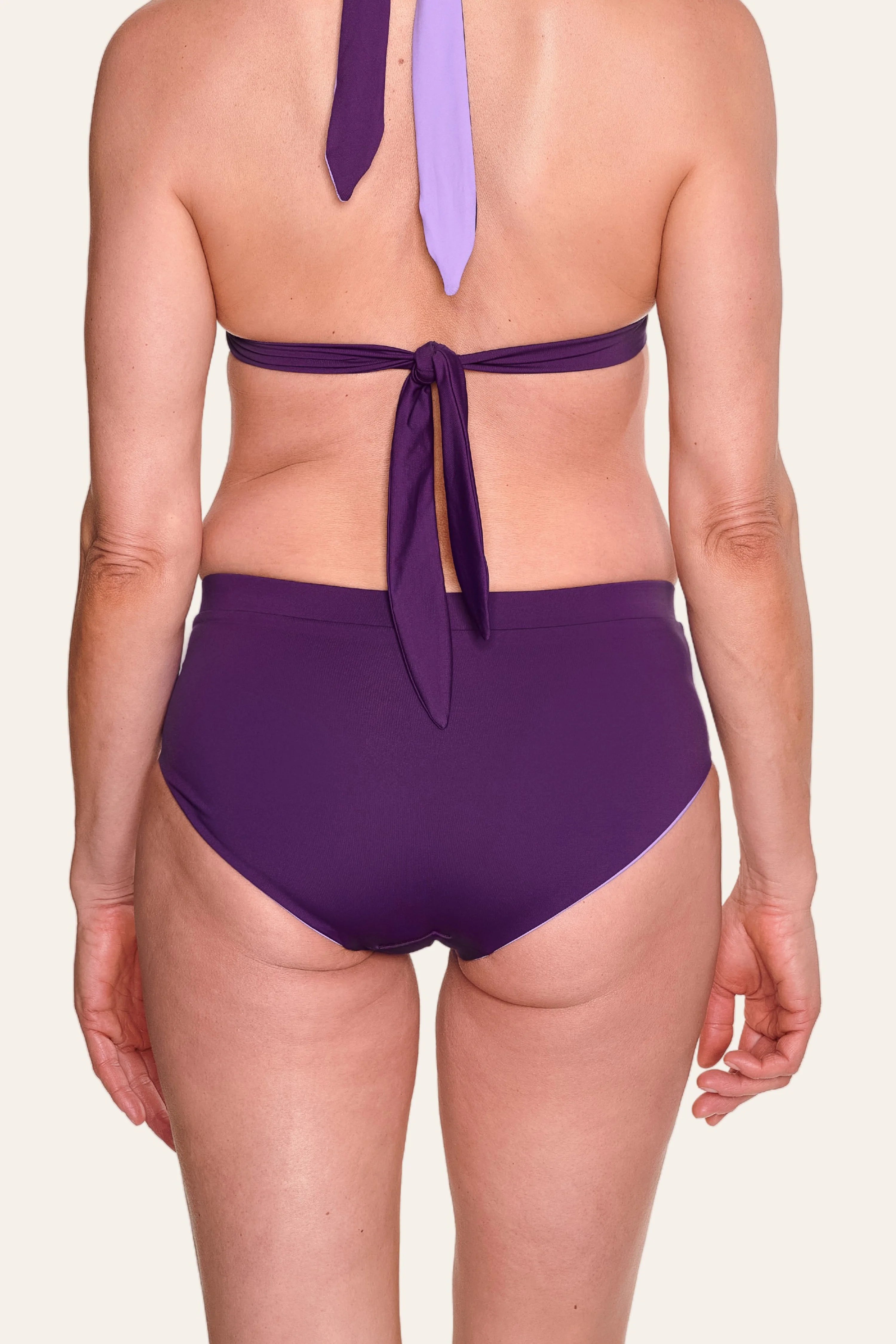 Rückansicht einer Person in MYMARINI Bikinihose mit hohem Beinausschnitt und Neckholder-Top in Lila.#color_lavender-plum