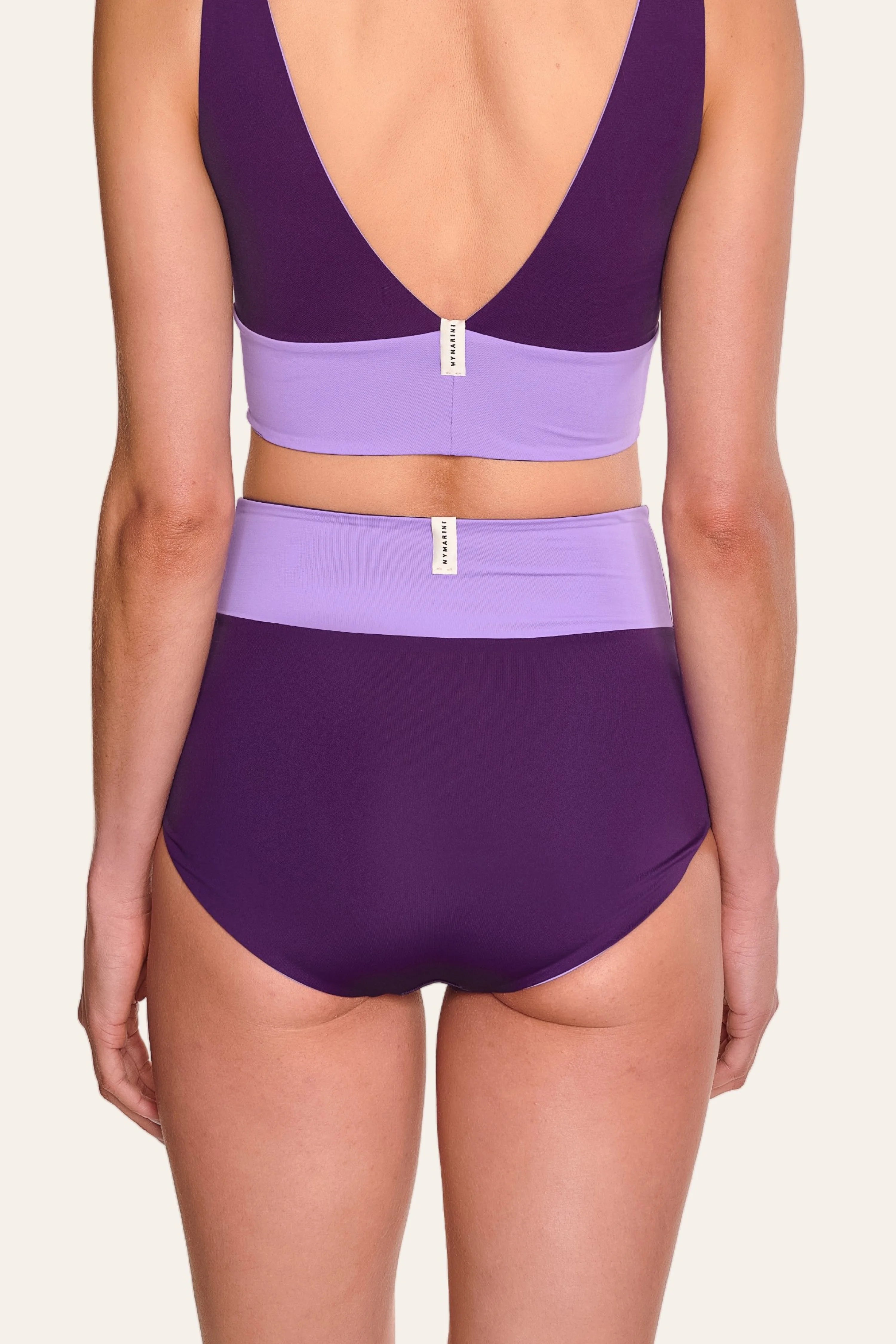 Rückenansicht einer Person in einem lila MYMARINI Bikinitop mit V-Ausschnitt und einer High-Waist-Bikinihose.#color_lavender-plum