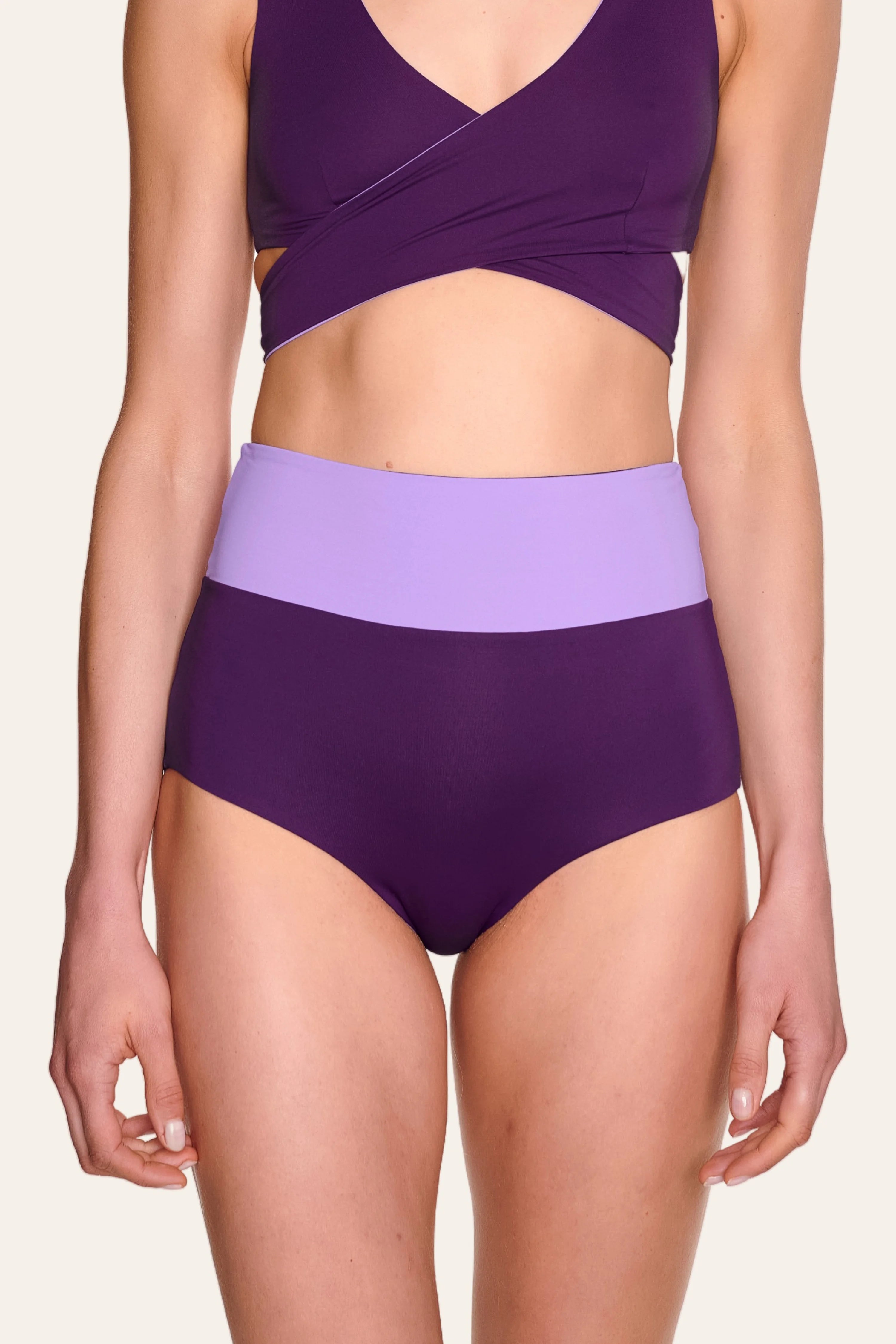 Frau trägt MYMARINI Bikinihose in Lila mit High Waist und passendem Cross Top.#color_lavender-plum