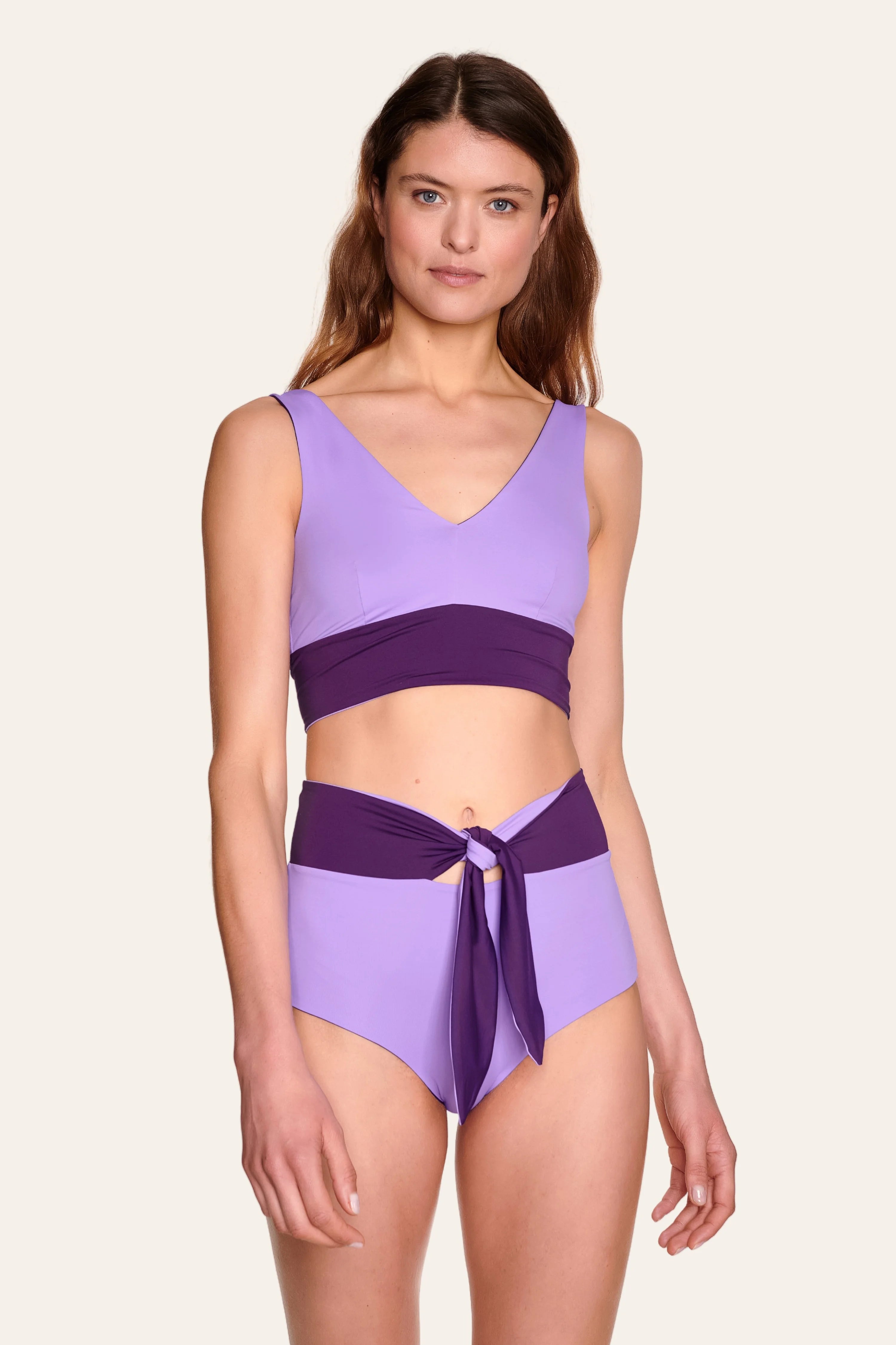 Frau trägt MYMARINI Bikini mit V-Ausschnitt und High-Waist-Schnitt in Lila und Dunkelviolett.#color_lavender-plum