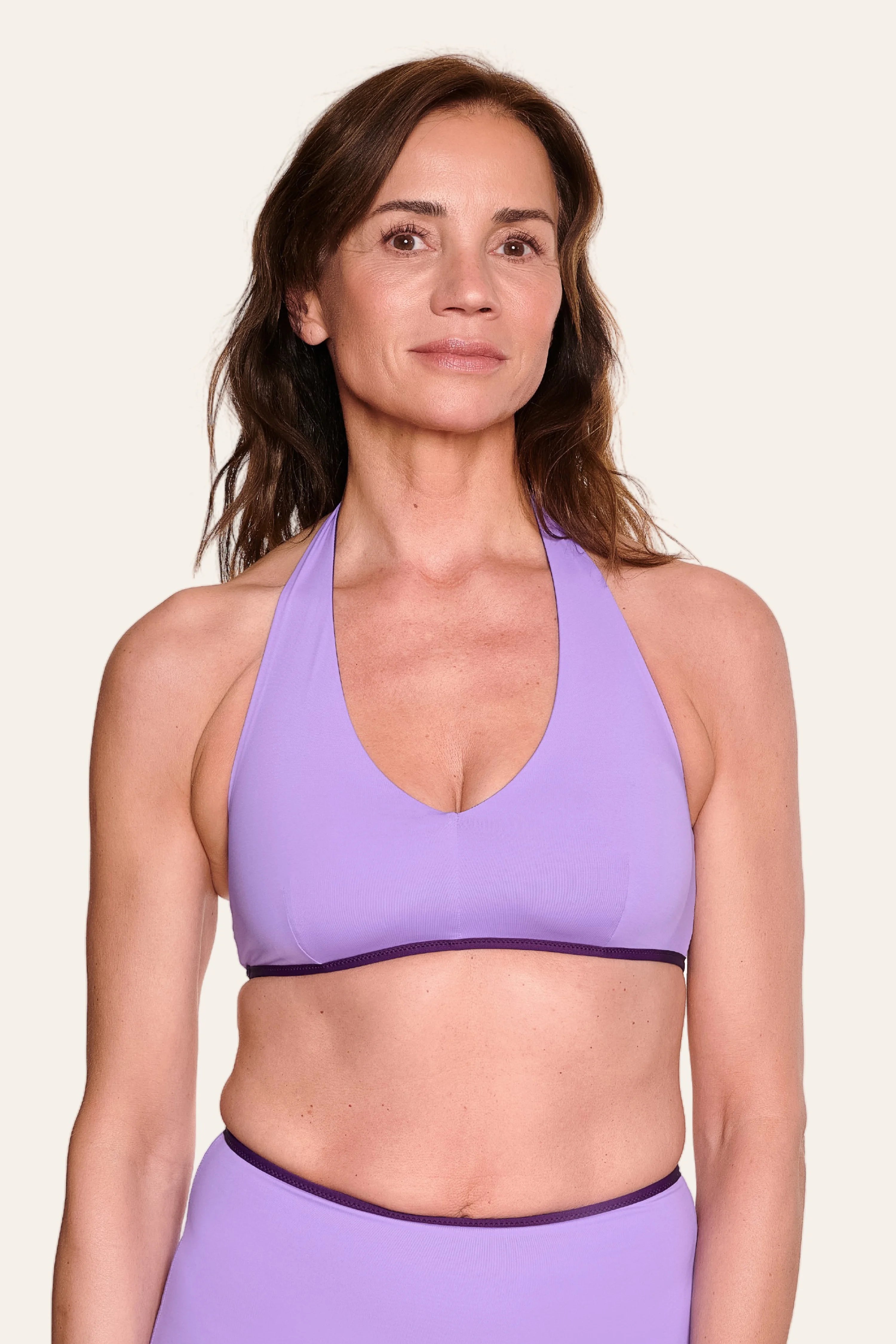 Frau trägt lila MYMARINI Neckholder-Bikinitop mit tiefem Ausschnitt vor hellem Hintergrund.#color_lavender-plum