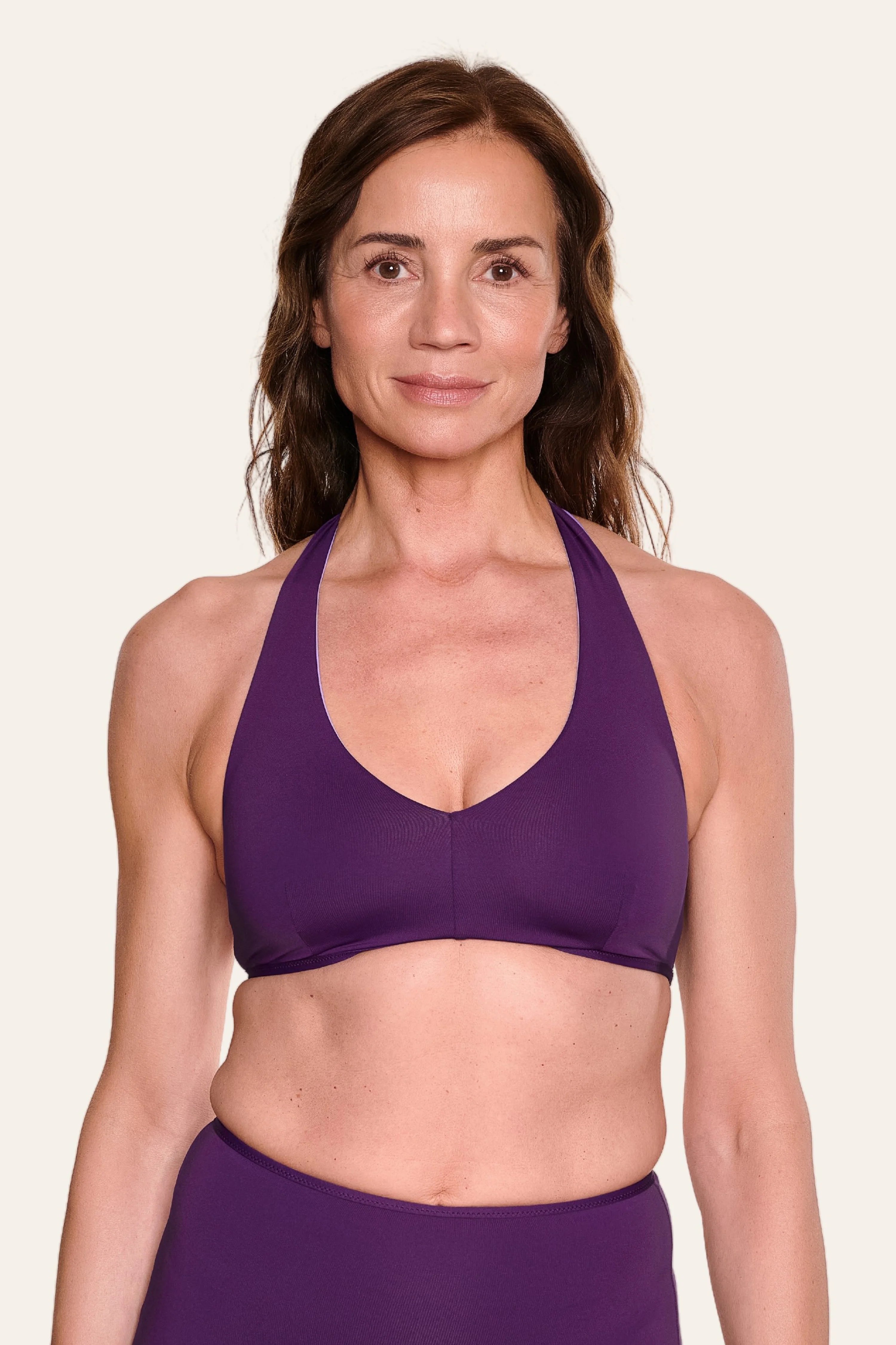 Frau trägt lila MYMARINI Bikinitop mit Neckholder-Schnitt vor hellem Hintergrund.#color_lavender-plum
