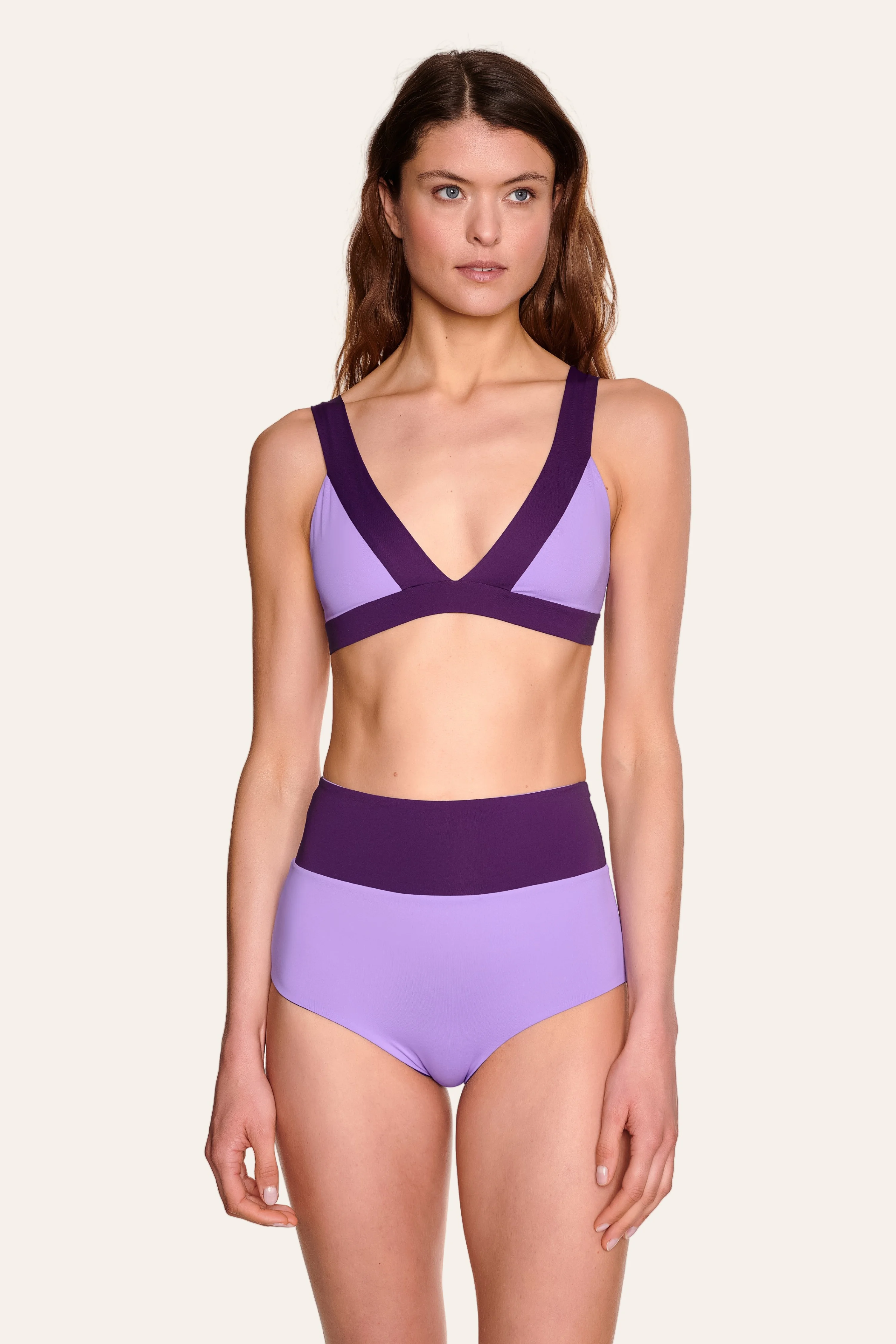 Frau trägt MYMARINI Bikini mit V-Ausschnitt und breiten Trägern in Lila, kombiniert mit einer High-Waist-Bikinihose.#color_lavender-plum