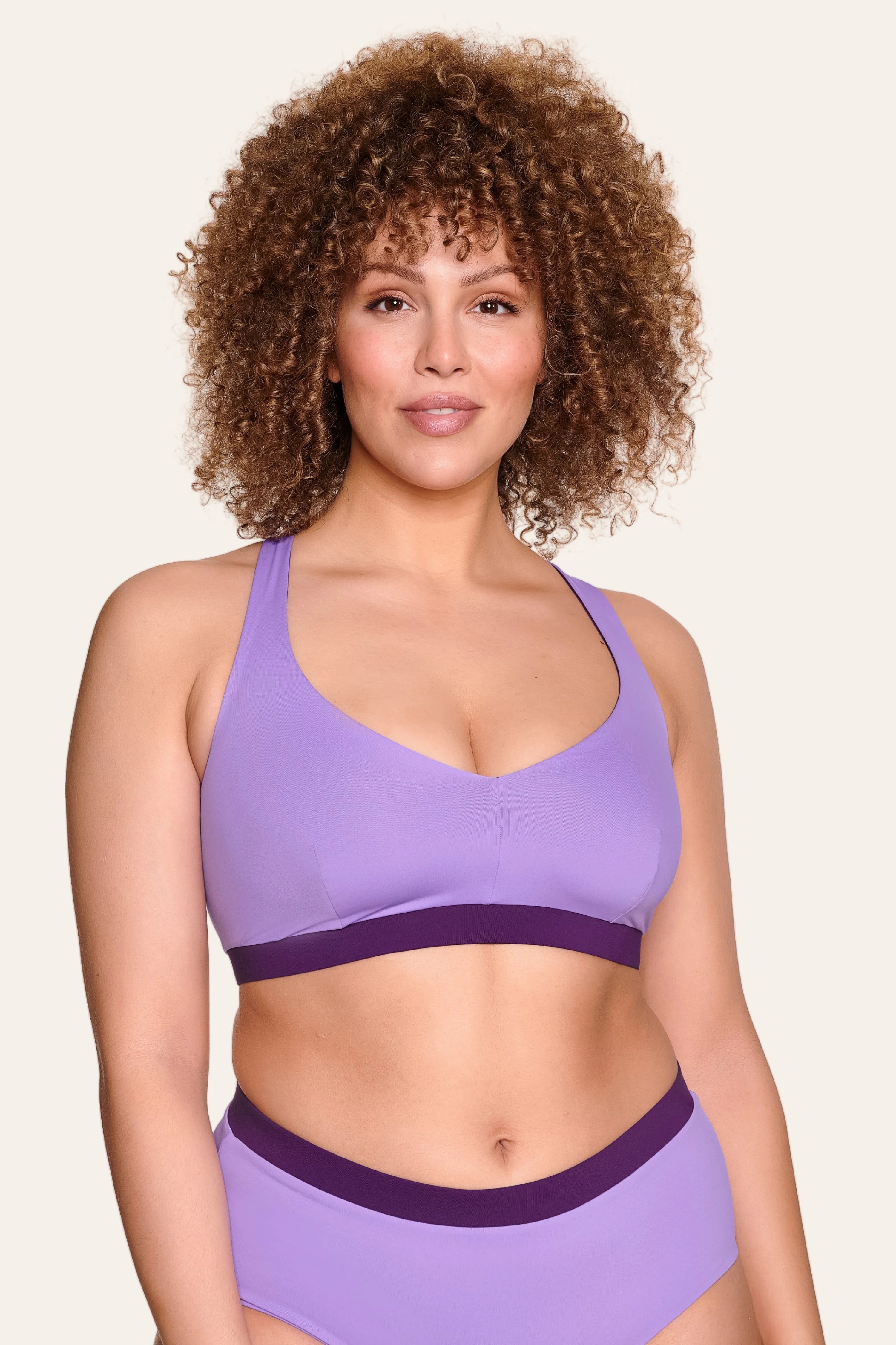 Frau trägt MYMARINI Bikinitop mit V-Ausschnitt und breite Träger in Lila, dazu passende Bikinihose.#color_lavender-plum