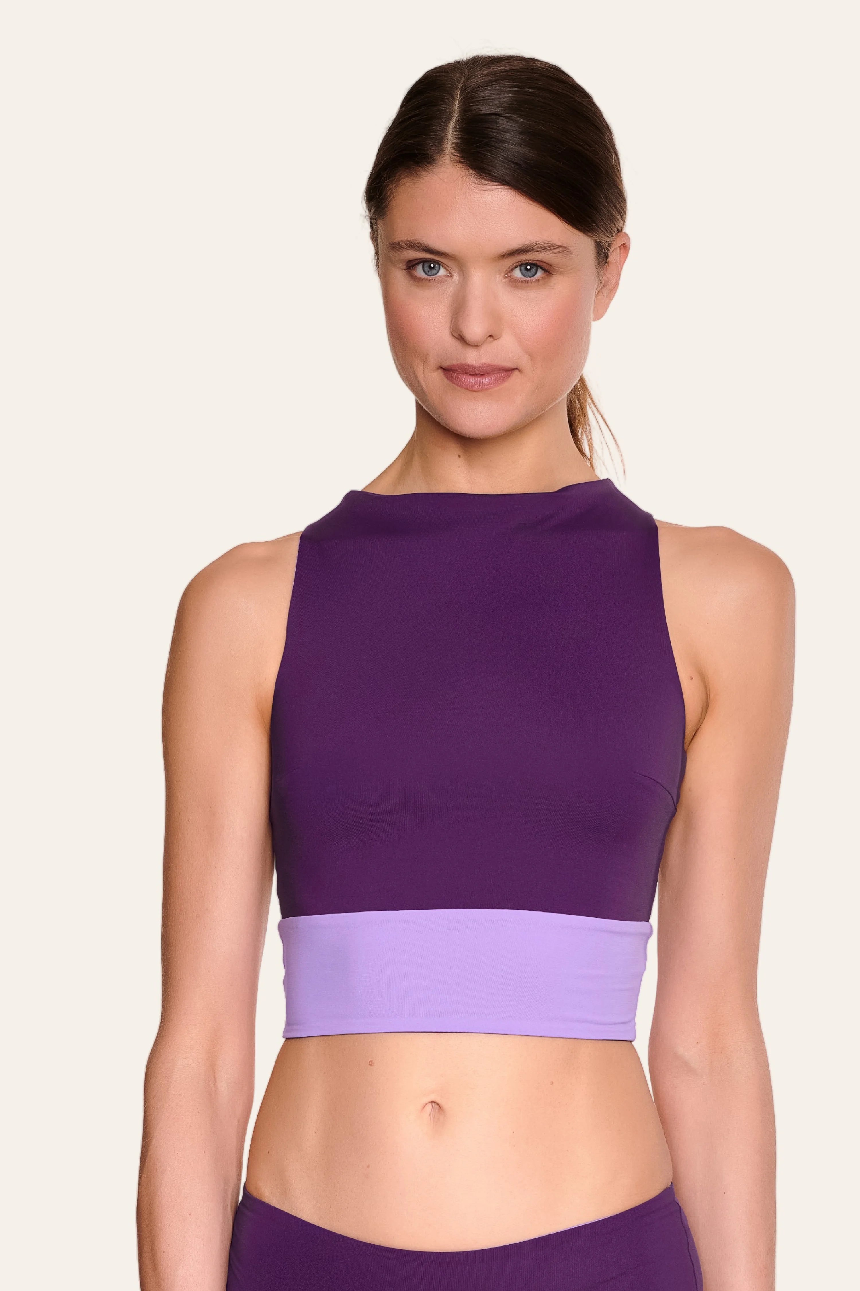 Frau trägt lila MYMARINI Bikinitop mit hoch geschlossenem Schnitt und breiten Trägern vor hellem Hintergrund.#color_lavender-plum