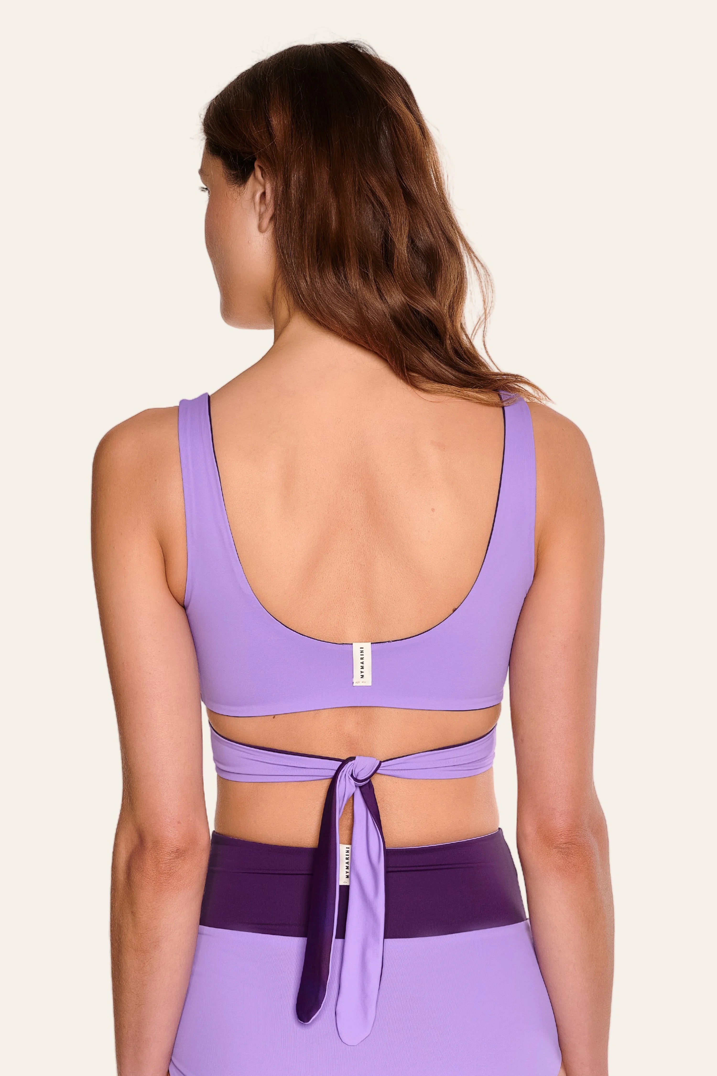 Frau trägt lila MYMARINI Bikinitop mit breiten Trägern und tiefem Rückenausschnitt, dazu passende Bikinihose.#color_lavender-plum