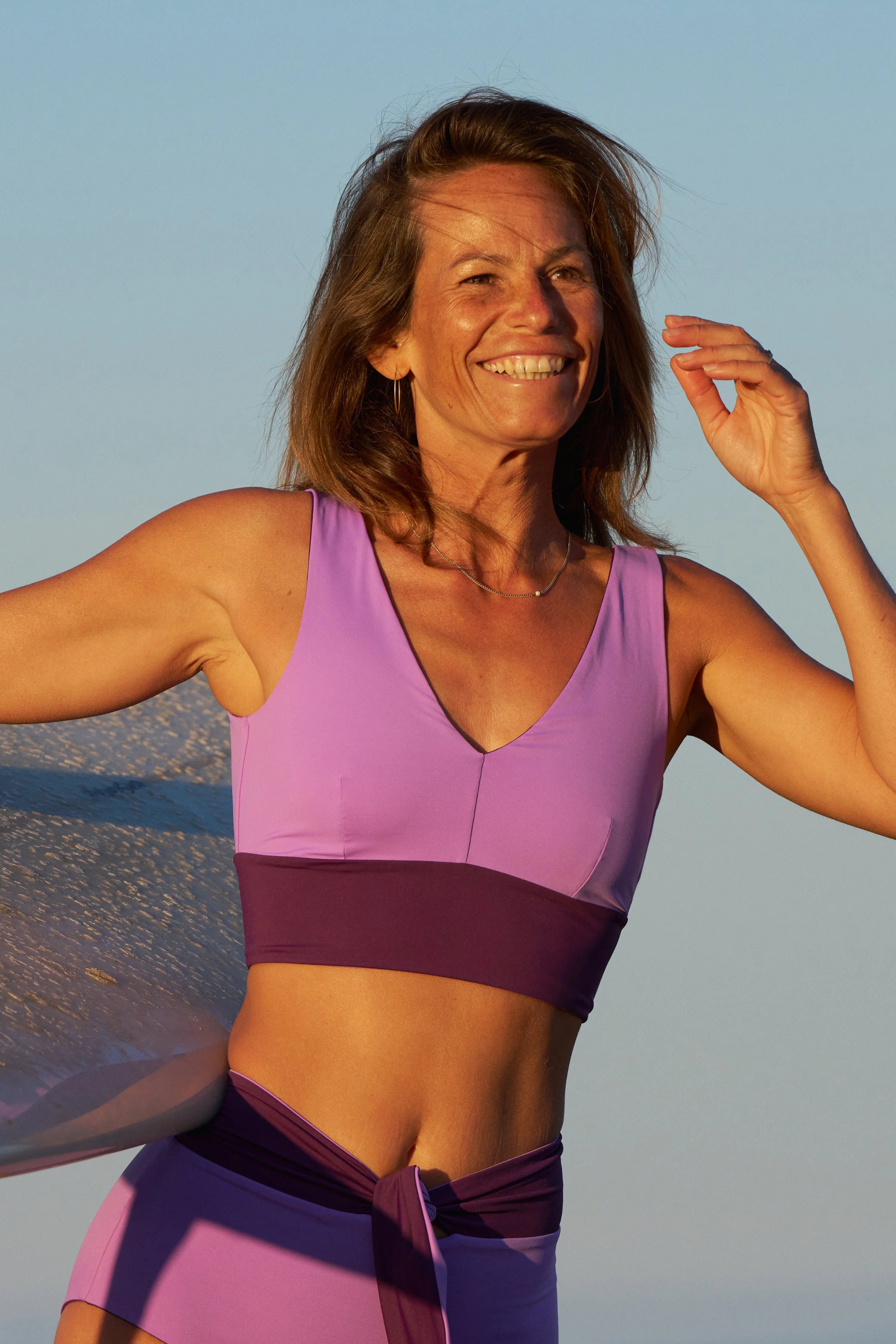 Frau in lila MYMARINI Bikinitop mit V-Ausschnitt und breiten Trägern, lächelnd am Strand.#color_lavender-plum