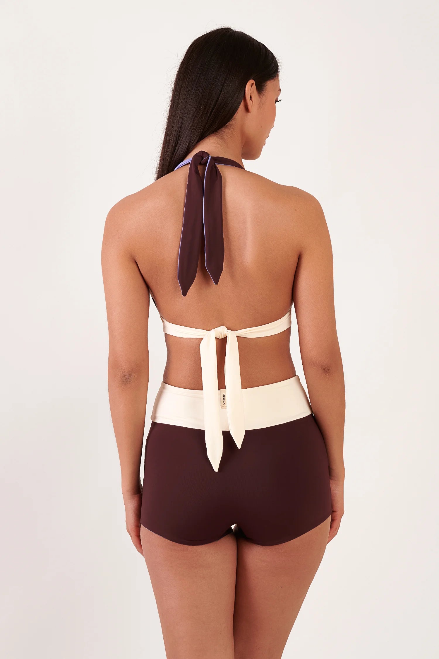 MYMARINI Bikini: Rückenansicht einer Frau mit Neckholder-Oberteil in Lila, weißem Rückengürtel, Bikinihose in Braun mit mittlerer Leibhöhe.#color_chocolate-lilac