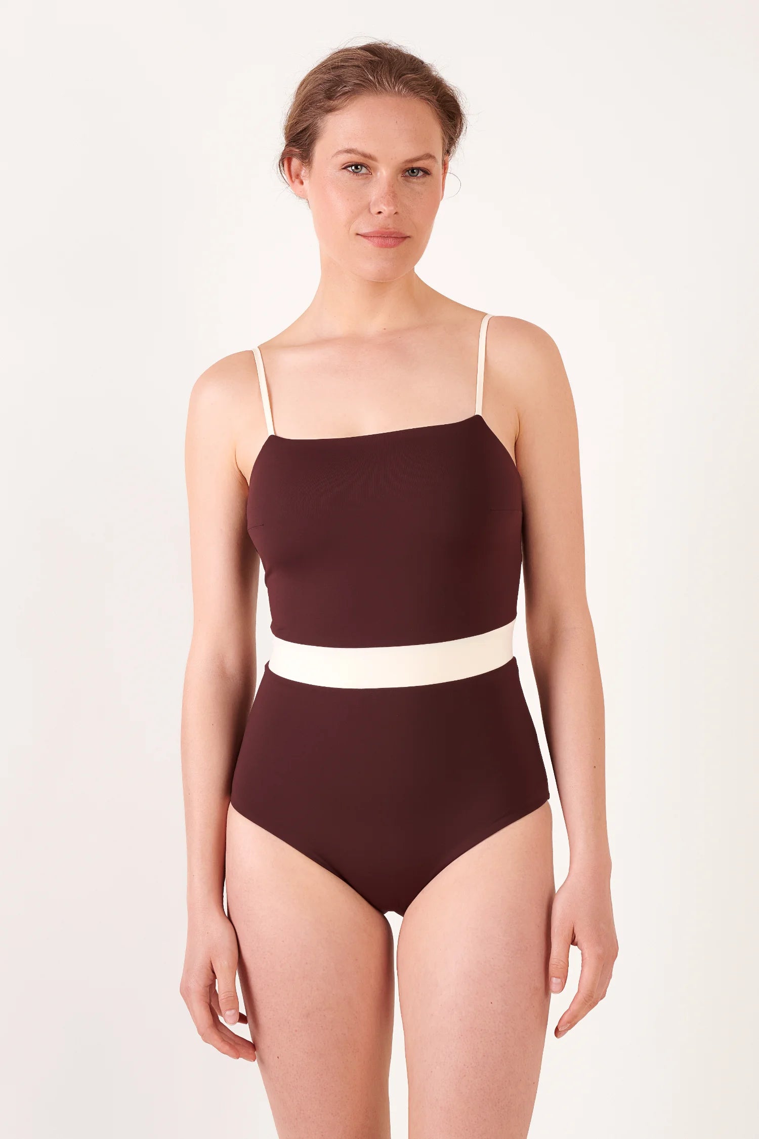 Modell zeigt einen dunkelbraunen MYMARINI One-Piece-Badeanzug mit cremefarbener Taillenschärpe; Spaghettiträger, gerader Oberteil.#color_chocolate-lilac