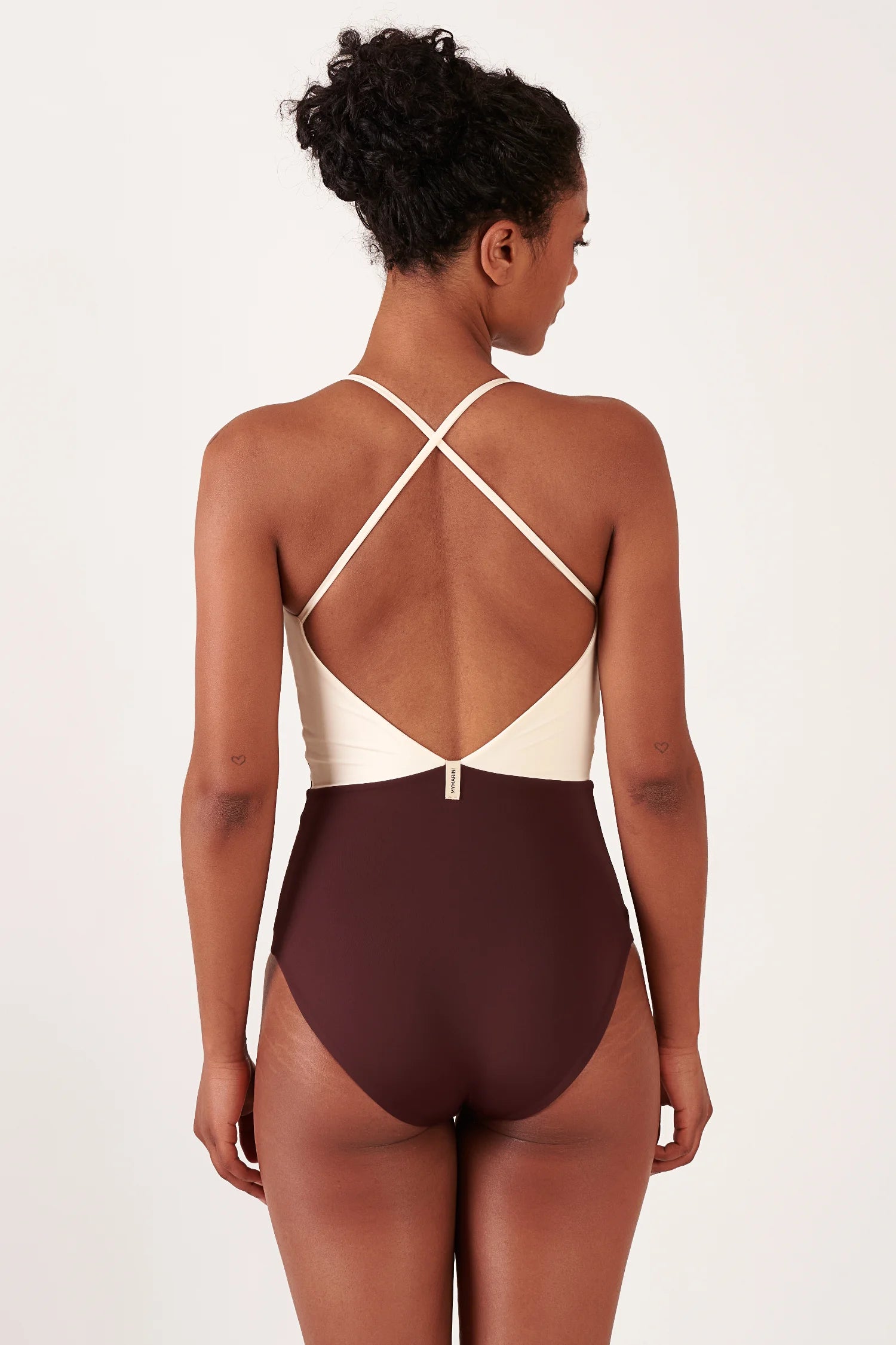 Frau von hinten in einem MYMARINI One-Piece-Badeanzug, cremefarbenes Oberteil mit kreuzenden Trägern und burgunderfarbener Unterteil.#color_chocolate-lilac