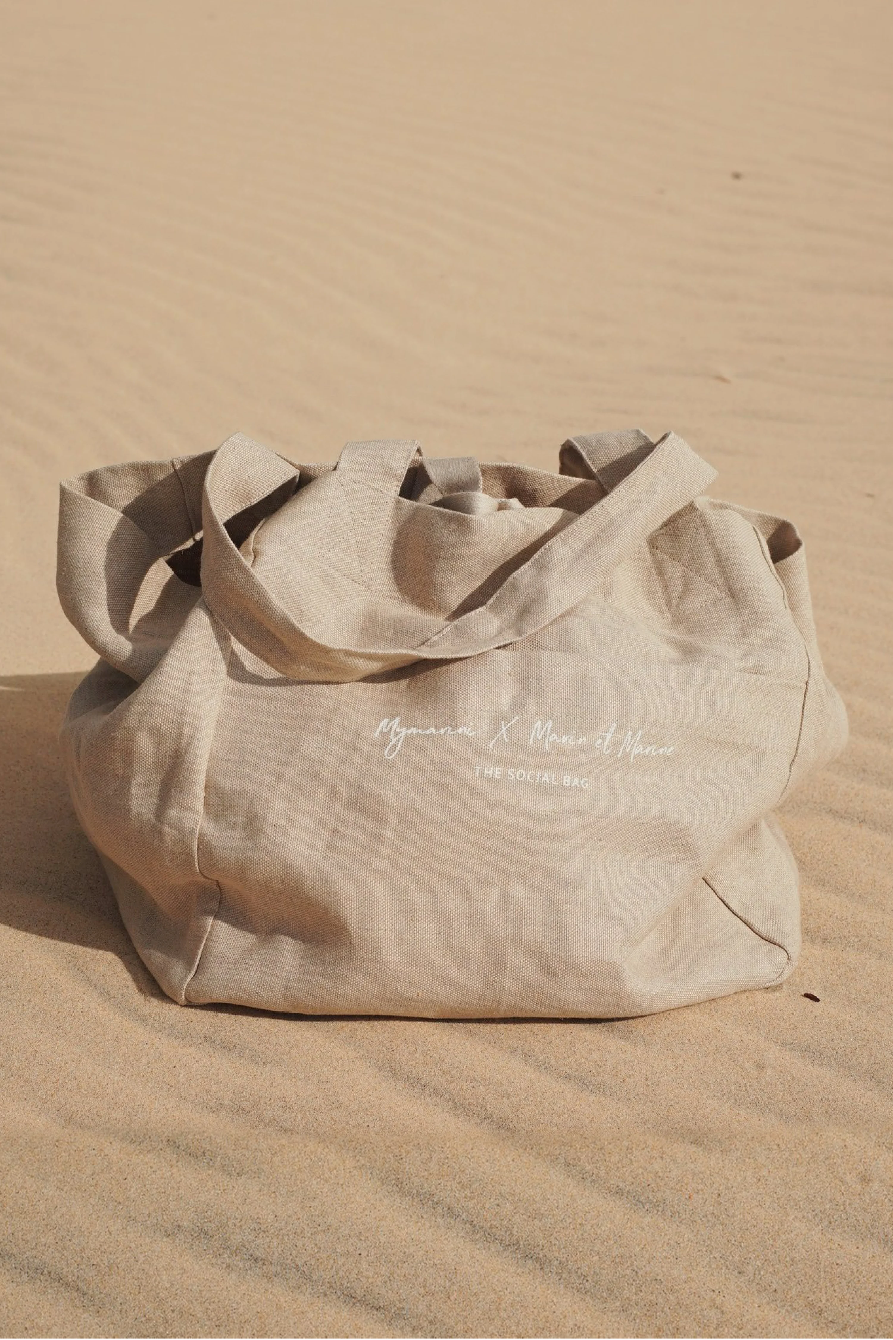 Beiger Stoffbeutel mit Aufschrift auf Sand.