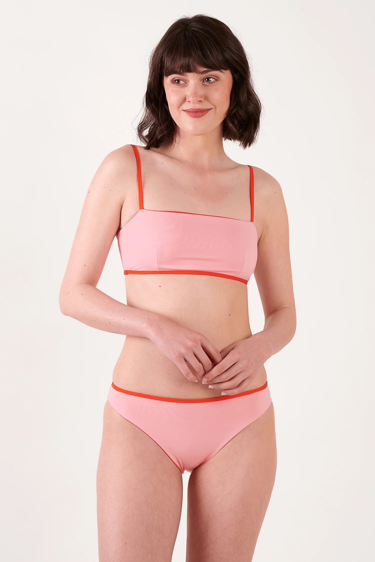 MYMARINI Bikini-Oberteil mit dünnen Trägern und rotem Rand; passende pinke Bikini-Hose mit rotem Bund, stehende Pose.#color_poppy-macaron
