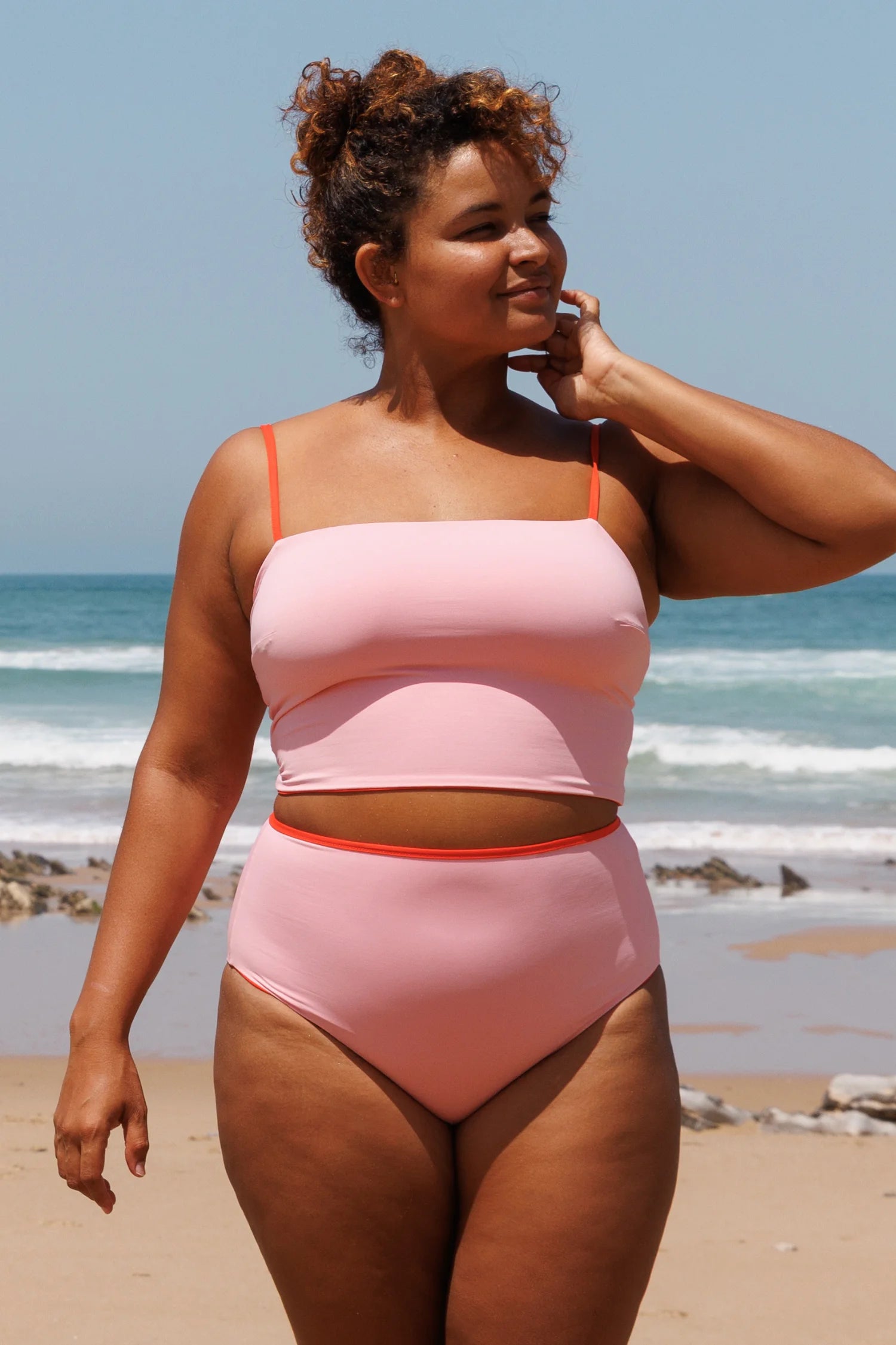 MYMARINI Bikini-Set: pinkes Oberteil mit Spaghettiträgern und hoher Bund der Hose, orangefarbene Akzente, am Strand.#color_poppy-macaron