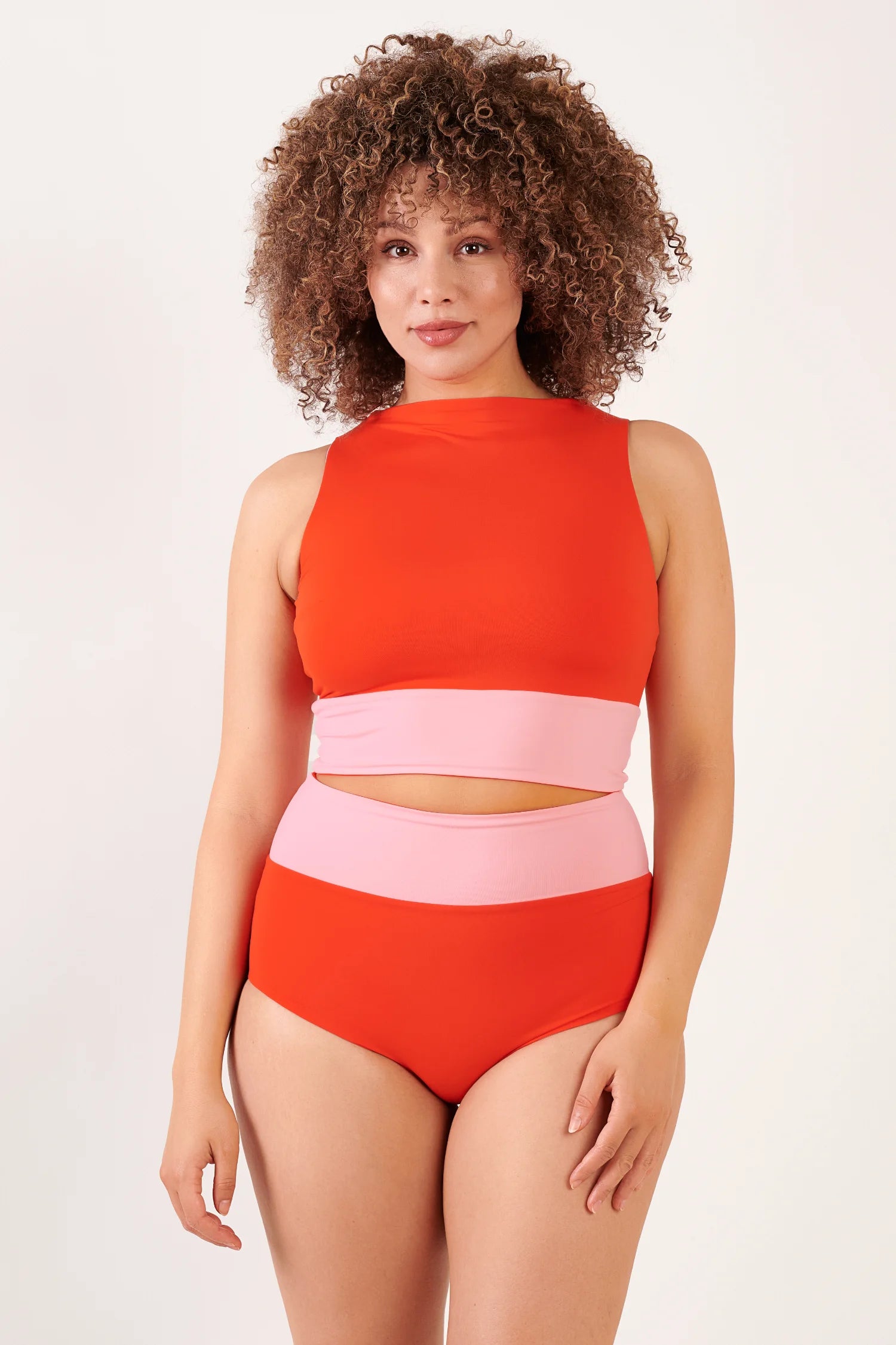 MYMARINI Bikini: Oberteil hochgeschlossen orange mit rosa Band; Bikinihose High-Waist orange mit rosa Bund; frontal stehende Person.#color_poppy-macaron