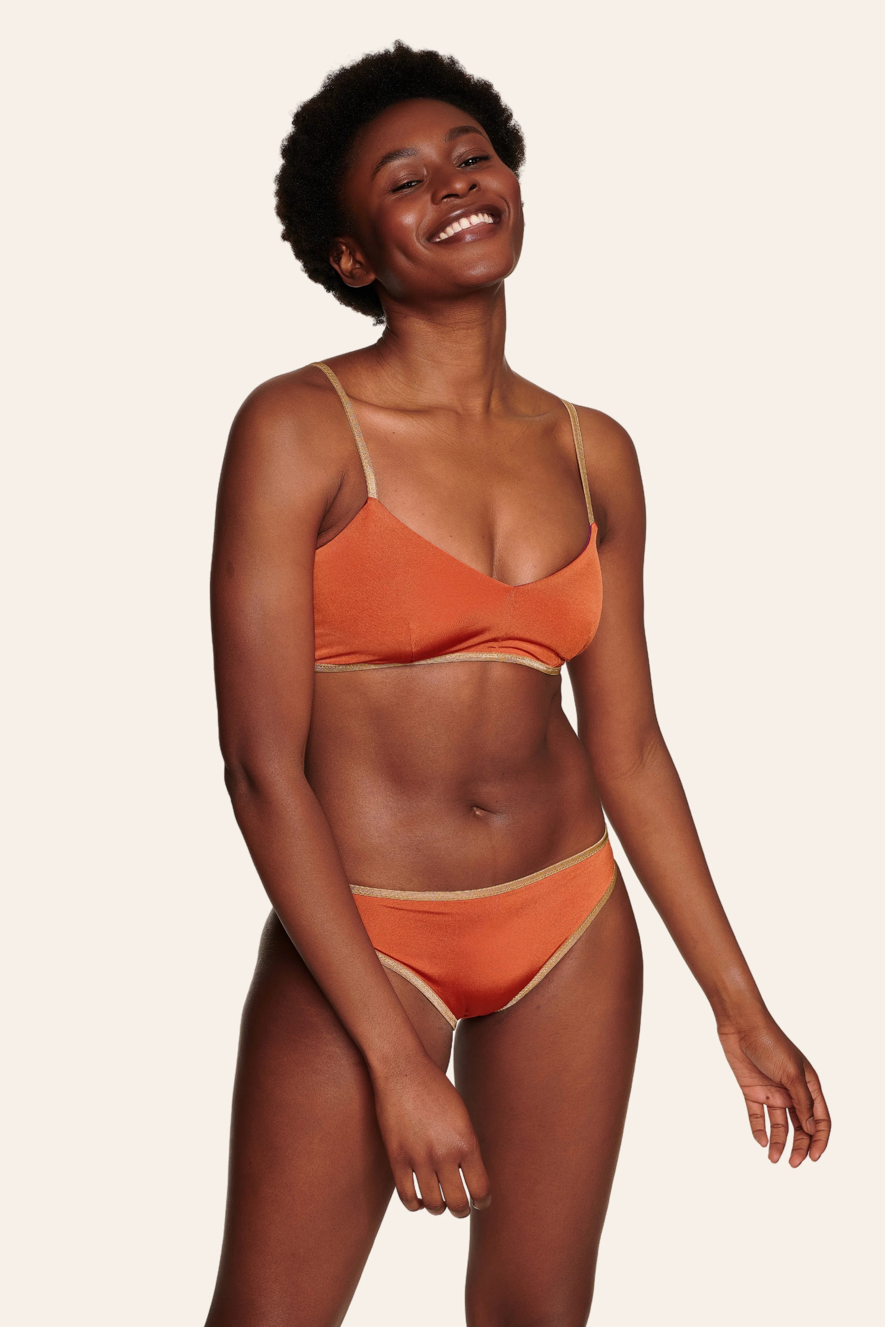 Lächelnde Person trägt MYMARINI Bikini mit Spaghettiträgern und hohem Beinausschnitt in Orange.#color_papaya-cassis