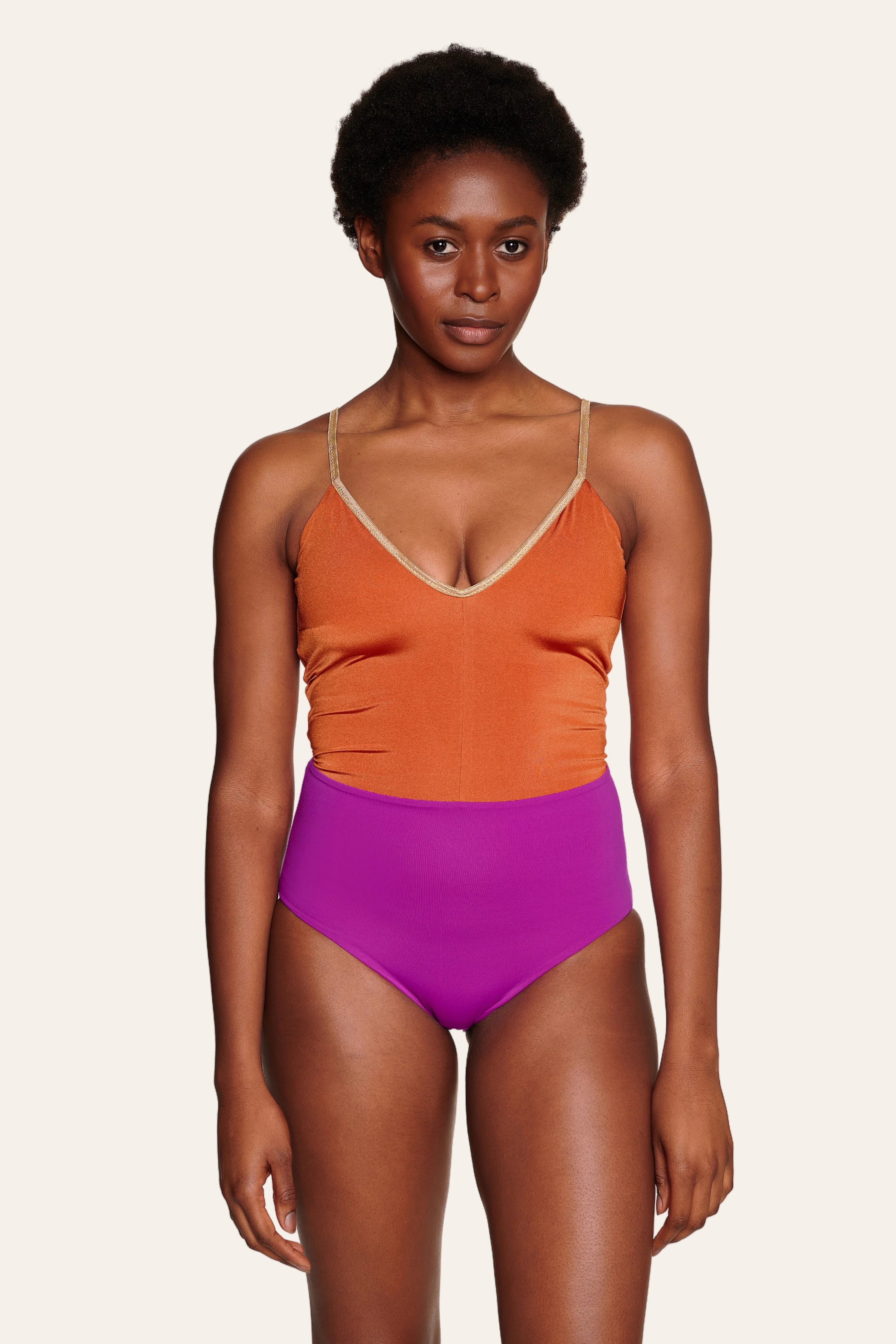 Person trägt einen MYMARINI Badeanzug mit V-Ausschnitt und Spaghettiträgern in Orange und Lila.#color_papaya-cassis