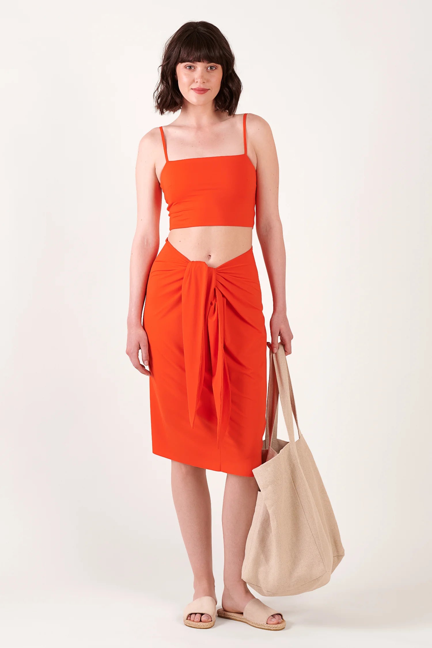 MYMARINI Top und Wickelrock in Orange; kurzes Top mit dünnen Trägern, Wickelrock vorne geknotet, beige Tasche in der Hand.#color_poppy