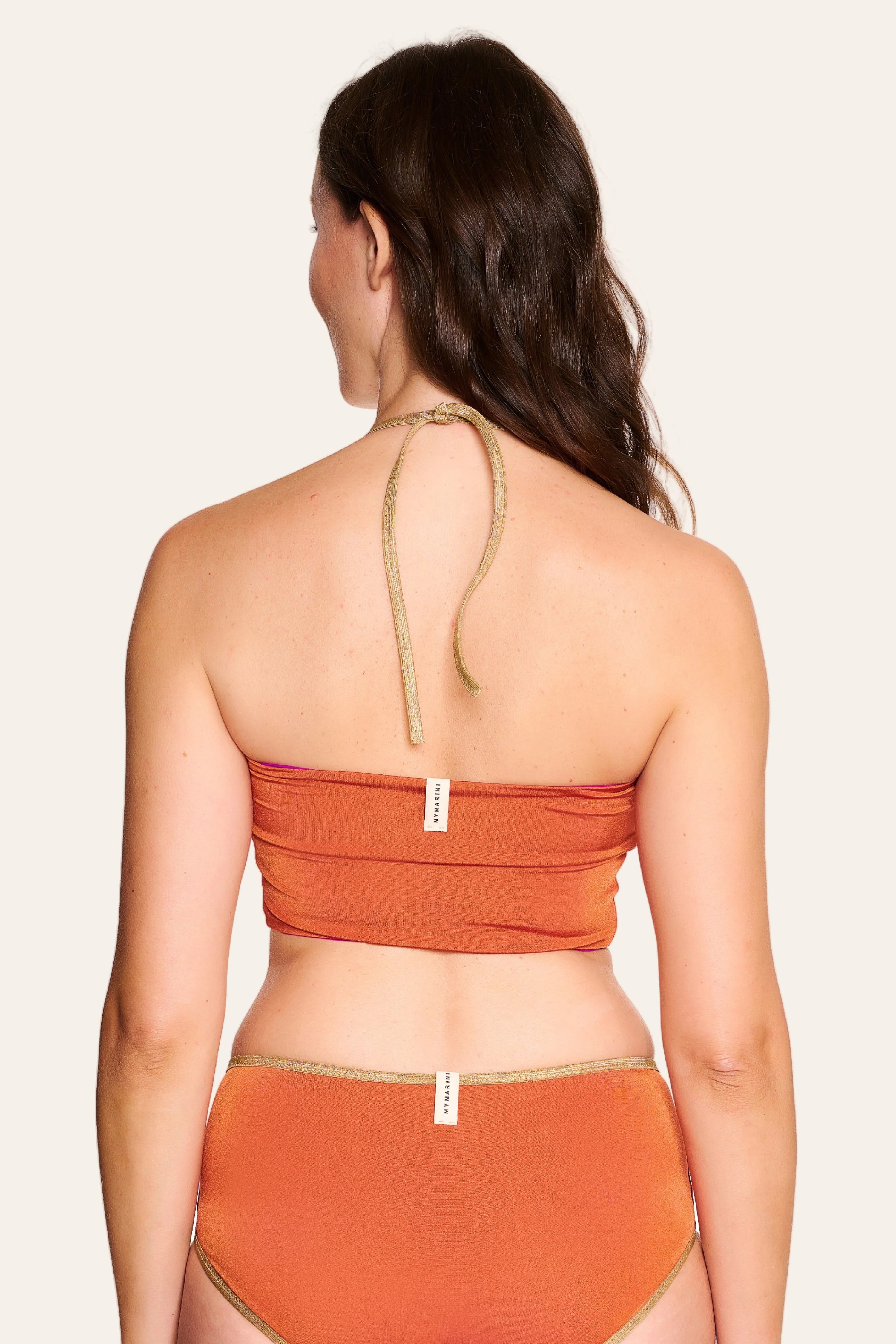Frau in MYMARINI Bikini mit Bandeau-Top und High-Waist-Hose in Orange, Rückansicht, vor hellem Hintergrund.#color_papaya-cassis