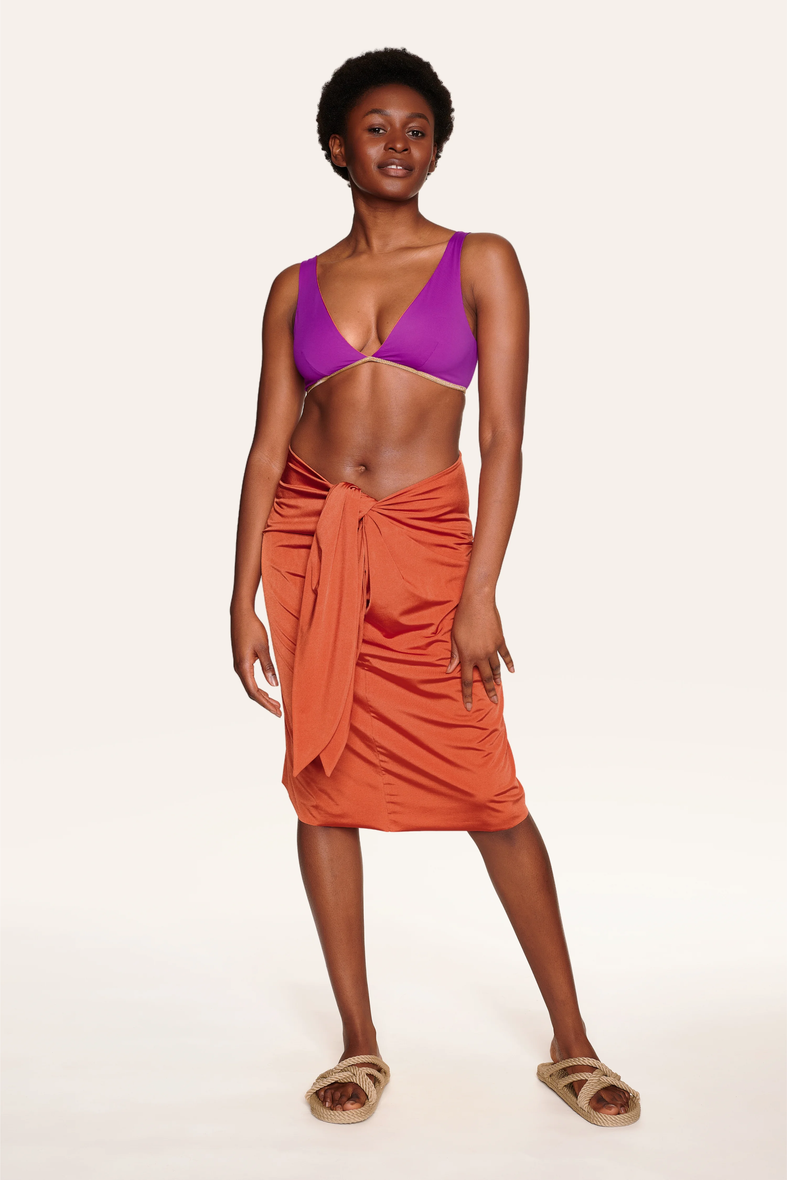 Frau trägt MYMARINI Bikinitop mit V-Ausschnitt und Rock. Sie steht lächelnd vor neutralem Hintergrund.#color_papaya