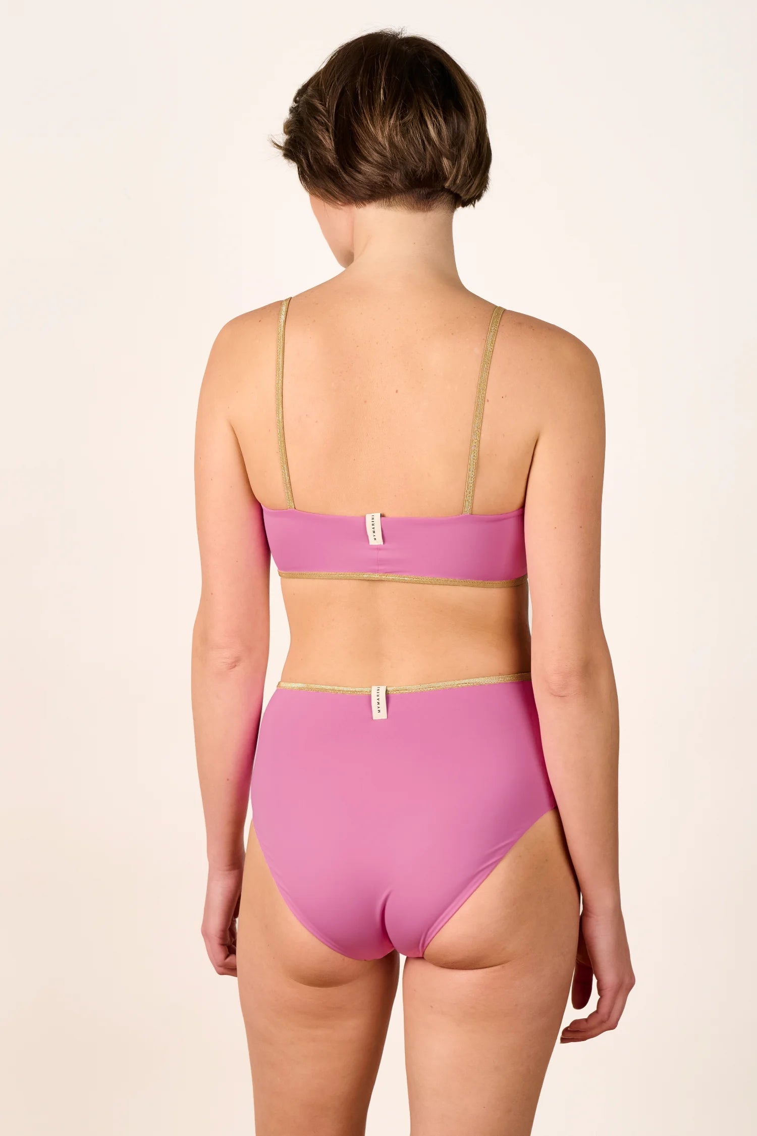 Rückansicht einer Person in einem pinken MYMARINI Bikini mit Spaghettiträgern und hohem Beinausschnitt.#color_bronze-orchid