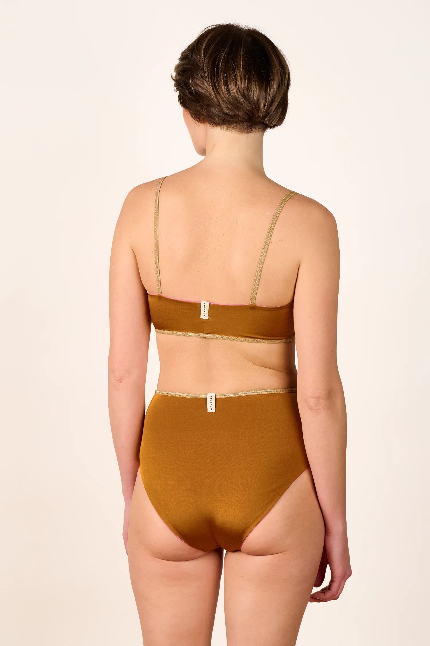 Rückansicht einer Person in einem MYMARINI Bikini mit Spaghettiträgern und hohem Beinausschnitt.#color_bronze-orchid