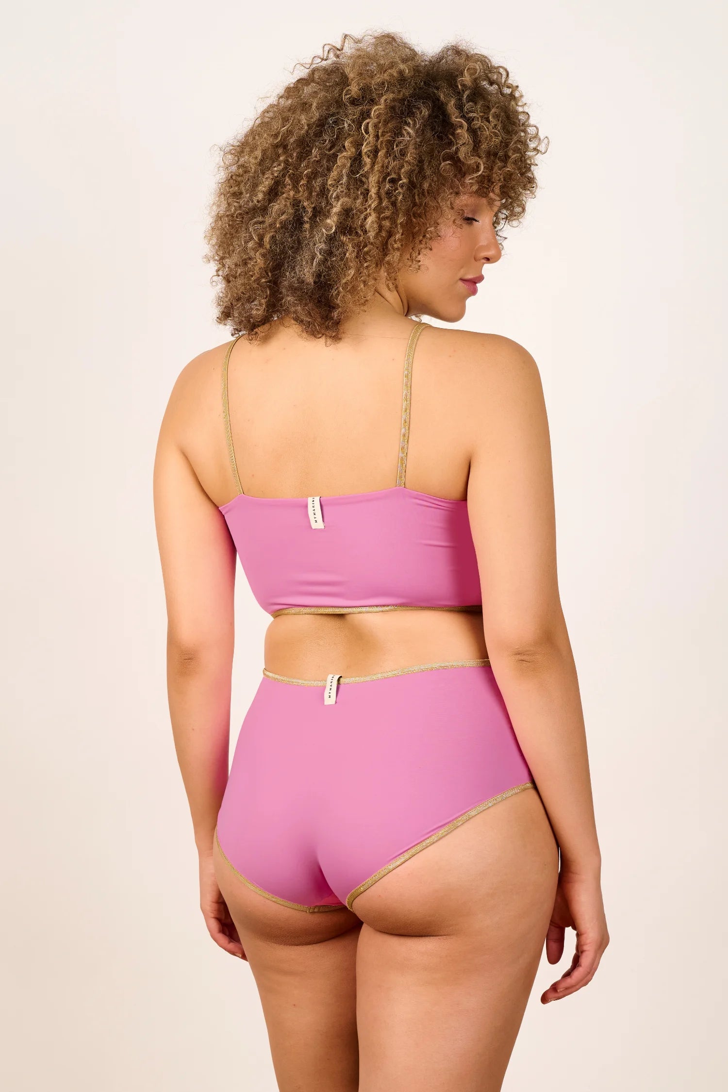 Frau trägt MYMARINI Bikini in Rosa mit Spaghettiträgern und hohem Beinausschnitt, Rückansicht.#color_bronze-orchid