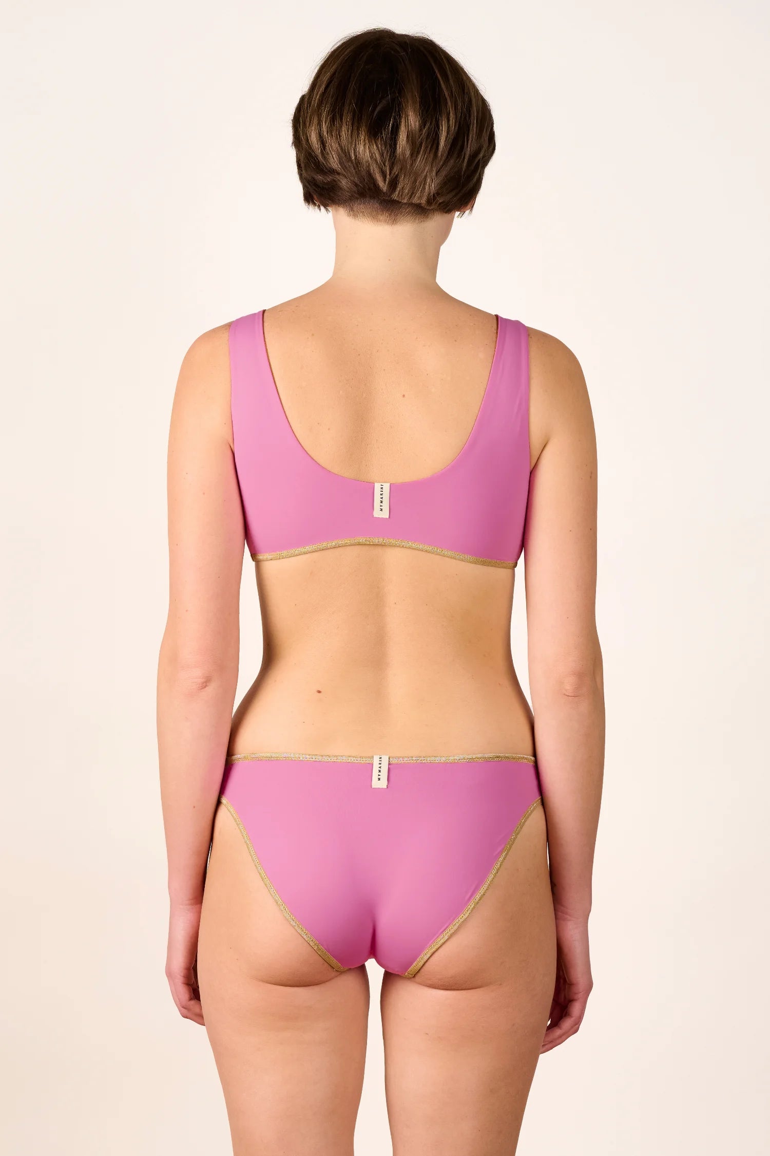 Rückansicht einer Person in einem rosa MYMARINI Bikini mit breiten Trägern und hohem Beinausschnitt.#color_bronze-orchid