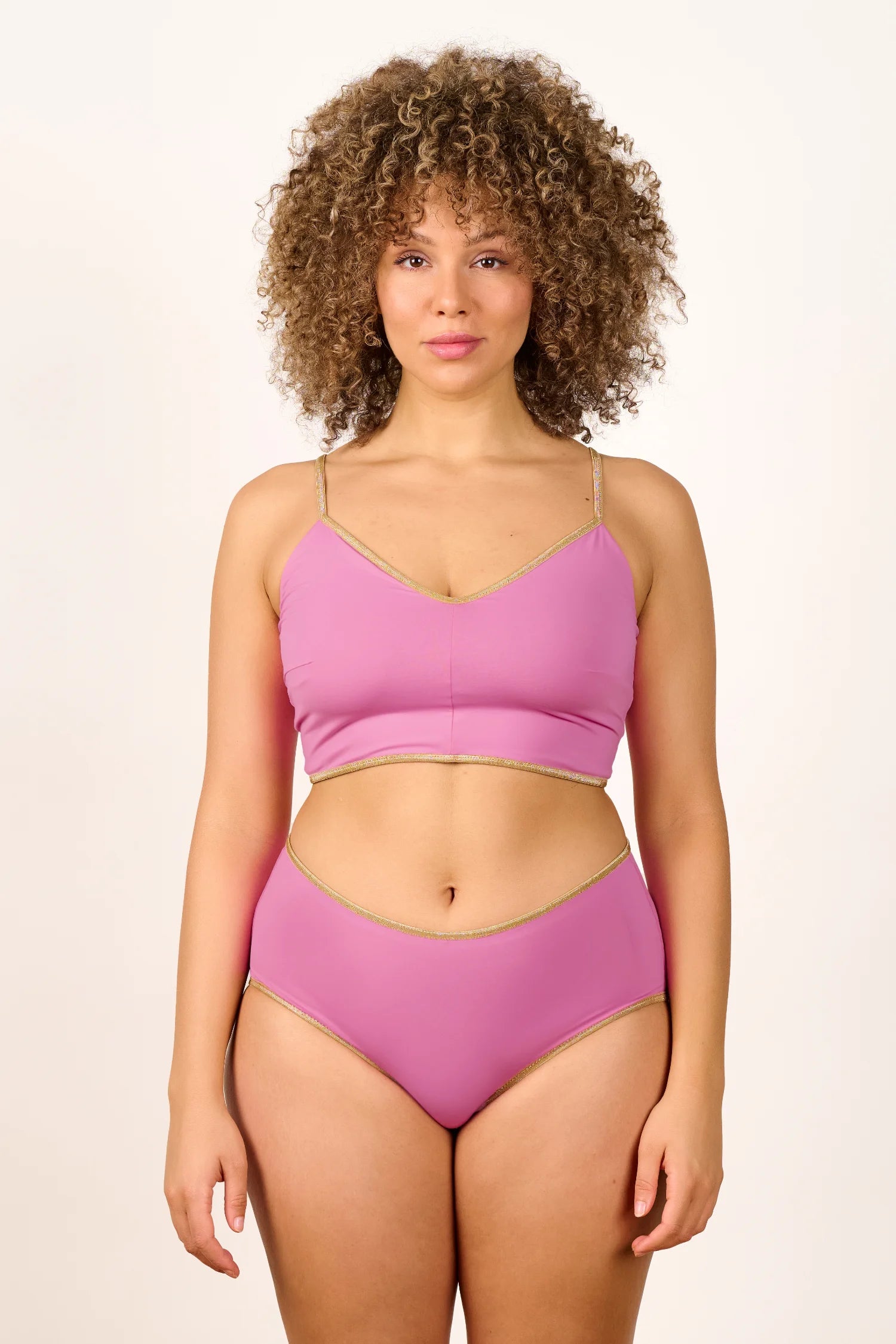 Frau trägt MYMARINI Bikini mit Spaghettiträgern und High Waist Schnitt in Rosa vor neutralem Hintergrund.#color_bronze-orchid
