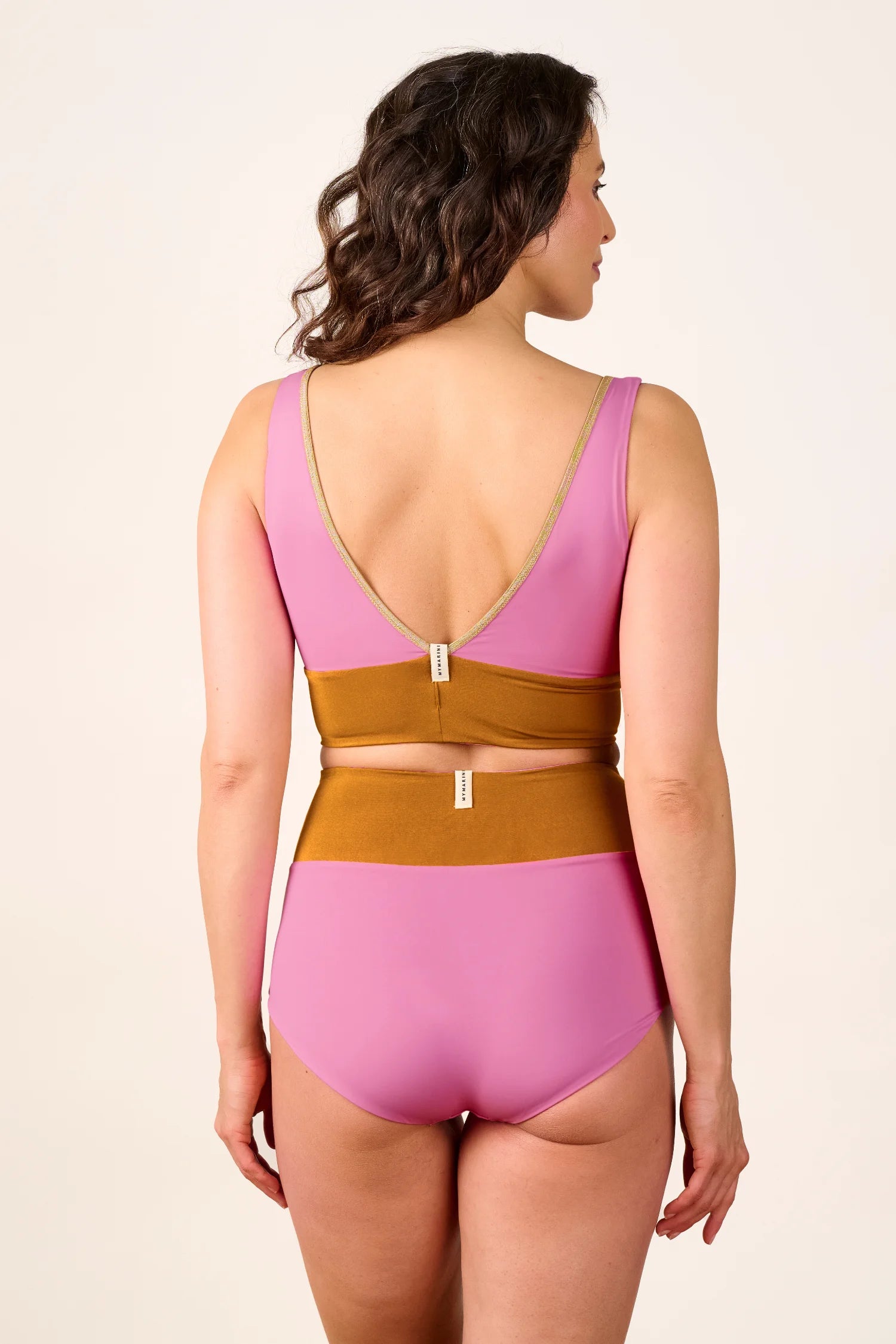 Frau trägt MYMARINI Badeanzug mit V-Ausschnitt und tiefem Rückenausschnitt in Rosa und Braun.#color_bronze-orchid