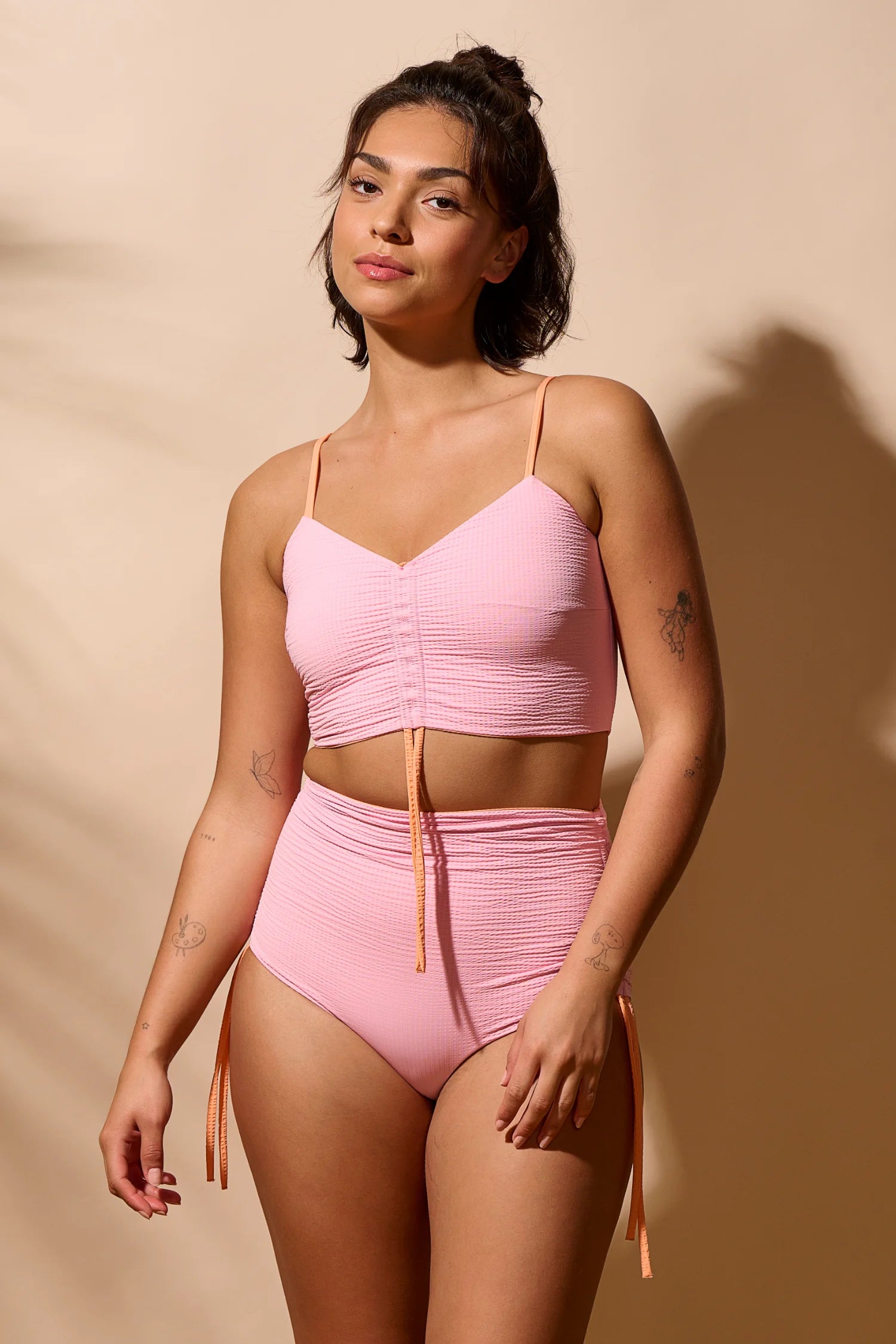 Frau in rosa MYMARINI Bikini mit Spaghettiträgern und High-Waist-Schnitt vor beigem Hintergrund.#color_marshmallow-peach