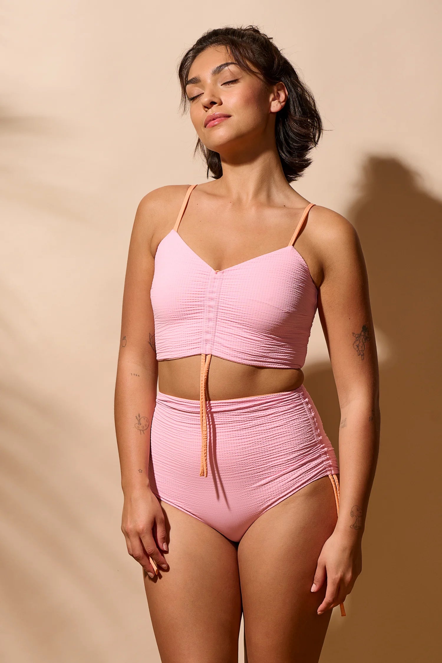 Frau trägt MYMARINI Bikini mit Spaghettiträgern und High Waist Schnitt in Rosa vor beigem Hintergrund.#color_marshmallow-peach