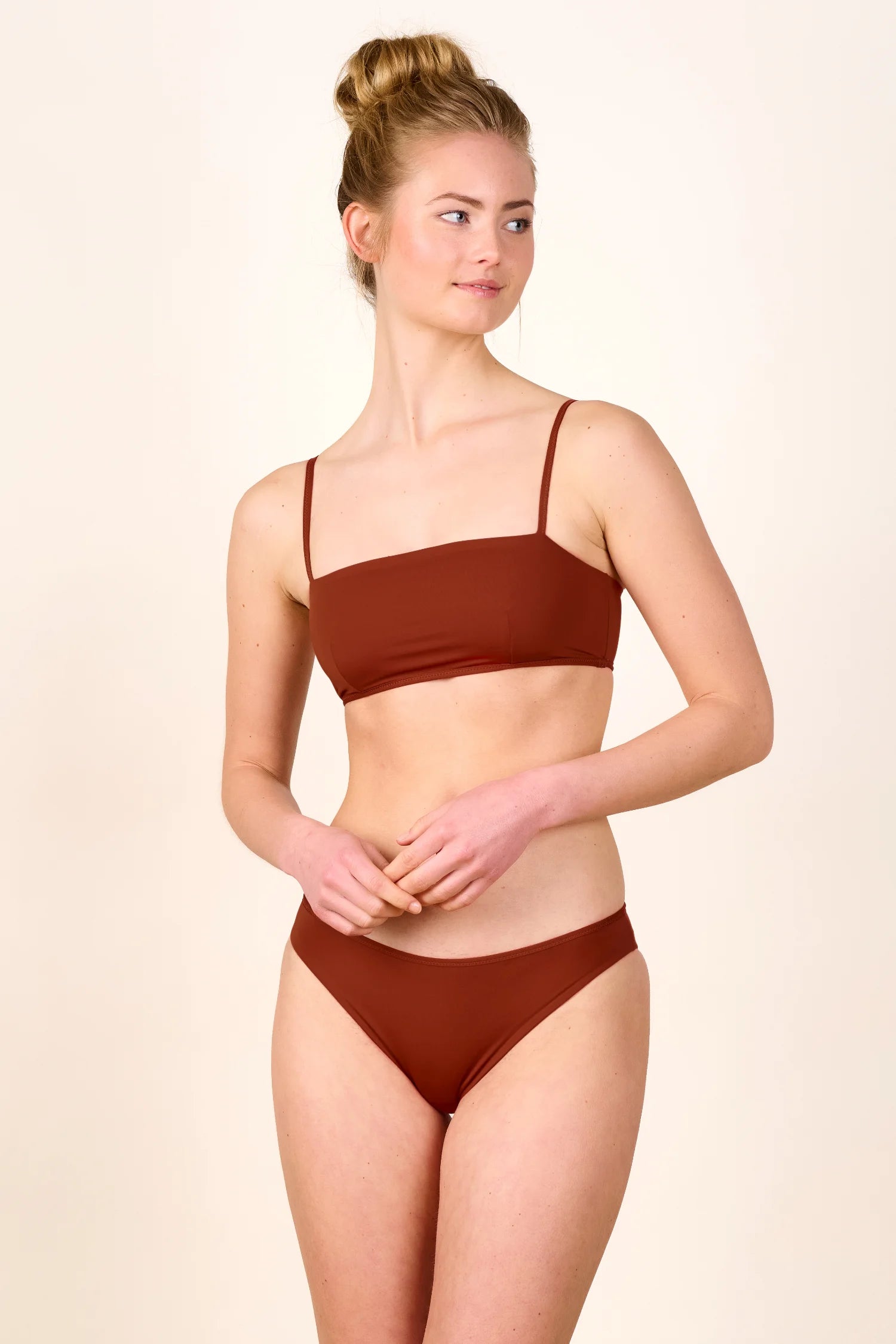 Frau trägt MYMARINI Bikini mit Spaghettiträgern und hohem Beinausschnitt in Braun, schaut nach rechts.#color_sienna-orchid