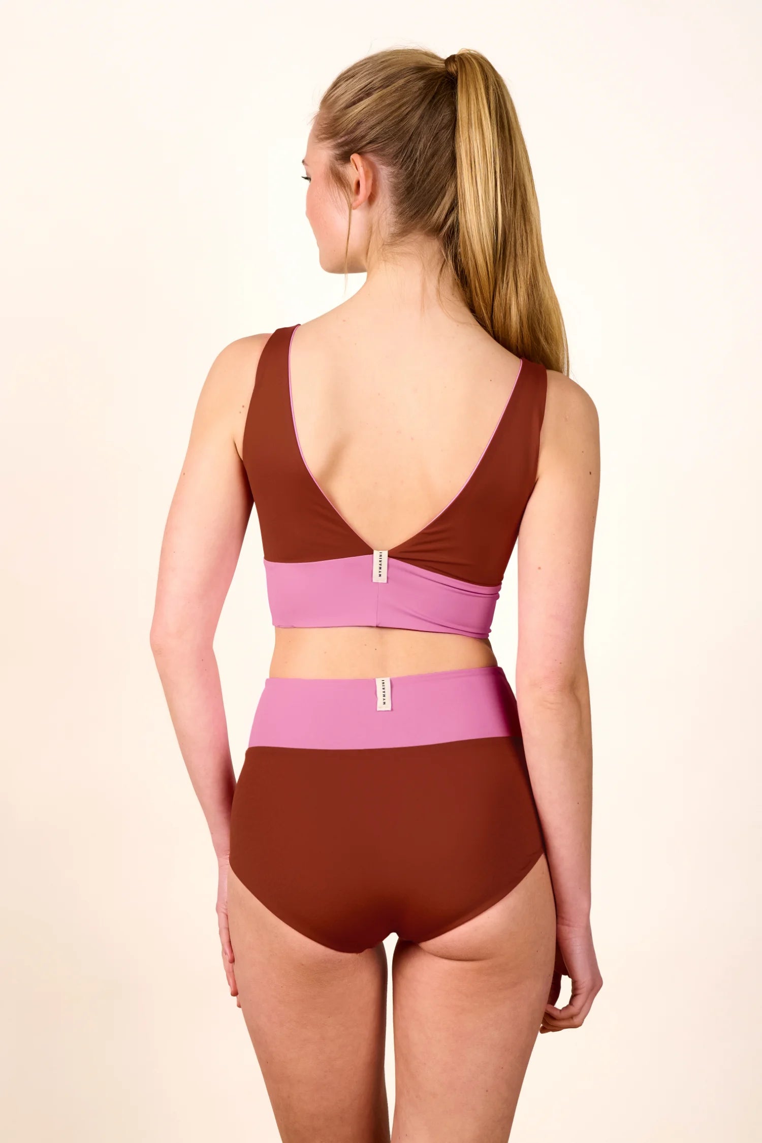 Frau trägt MYMARINI Bikini mit V-Ausschnitt und hohem Beinausschnitt in Braun und Rosa, Rückansicht.#color_sienna-orchid