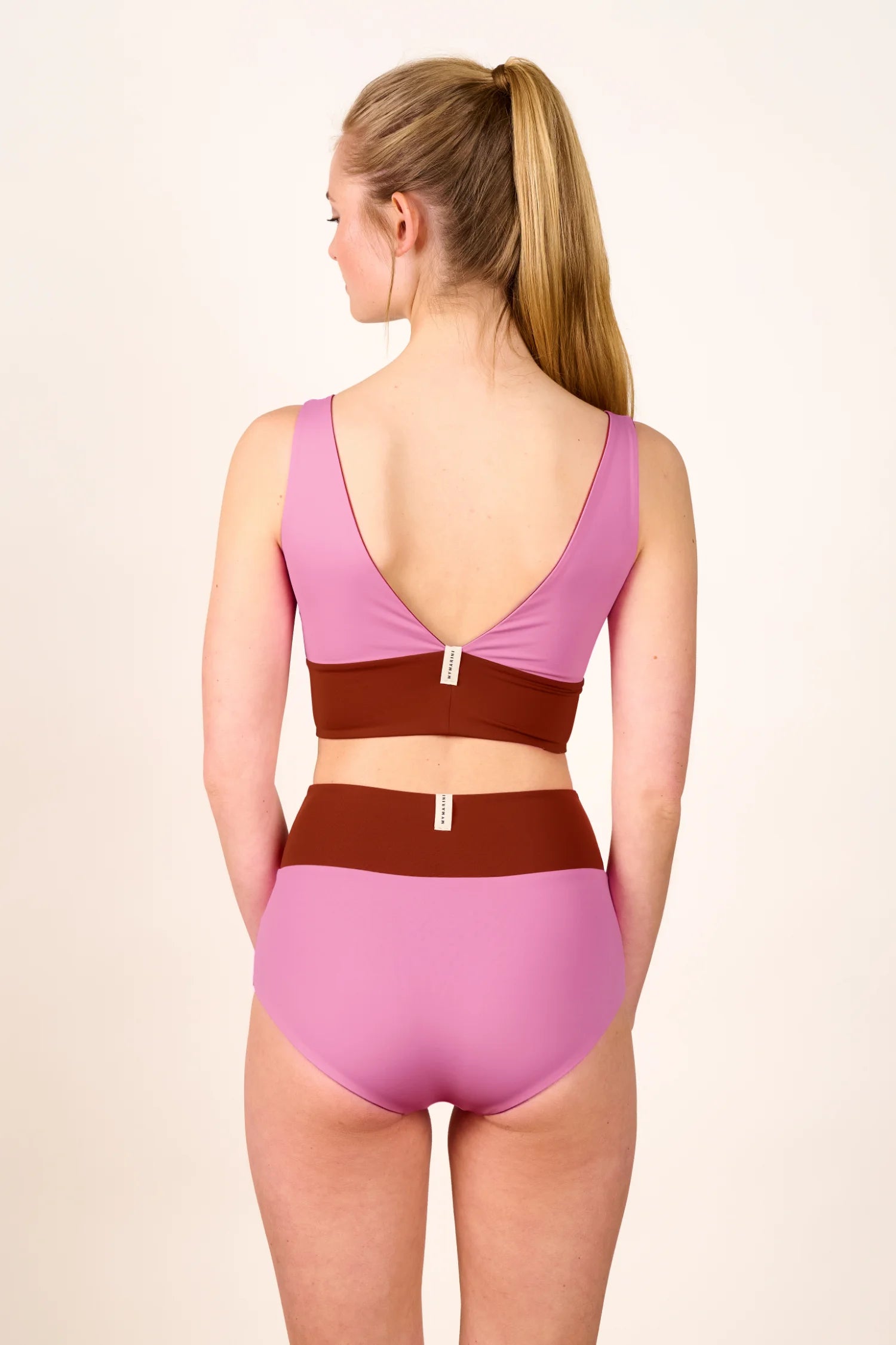 Frau in rosa-braunem MYMARINI-Bikini mit V-Ausschnitt und hohem Beinausschnitt, von hinten gezeigt.#color_sienna-orchid