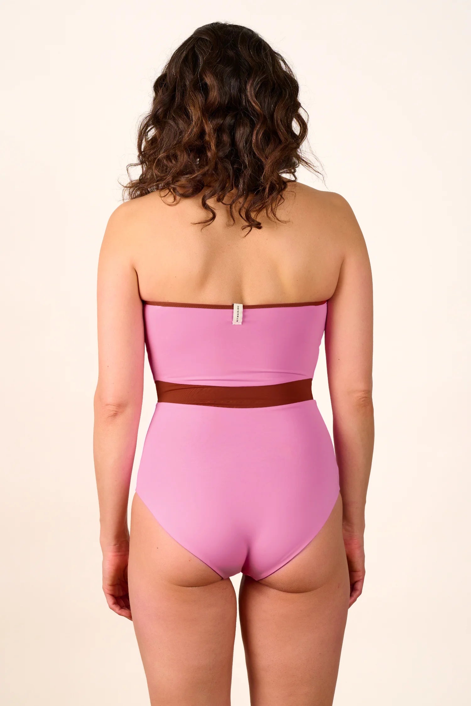 Frau in rosa MYMARINI-Badeanzug mit Bandeau-Schnitt und hohem Beinausschnitt, Rückansicht.#color_sienna-orchid