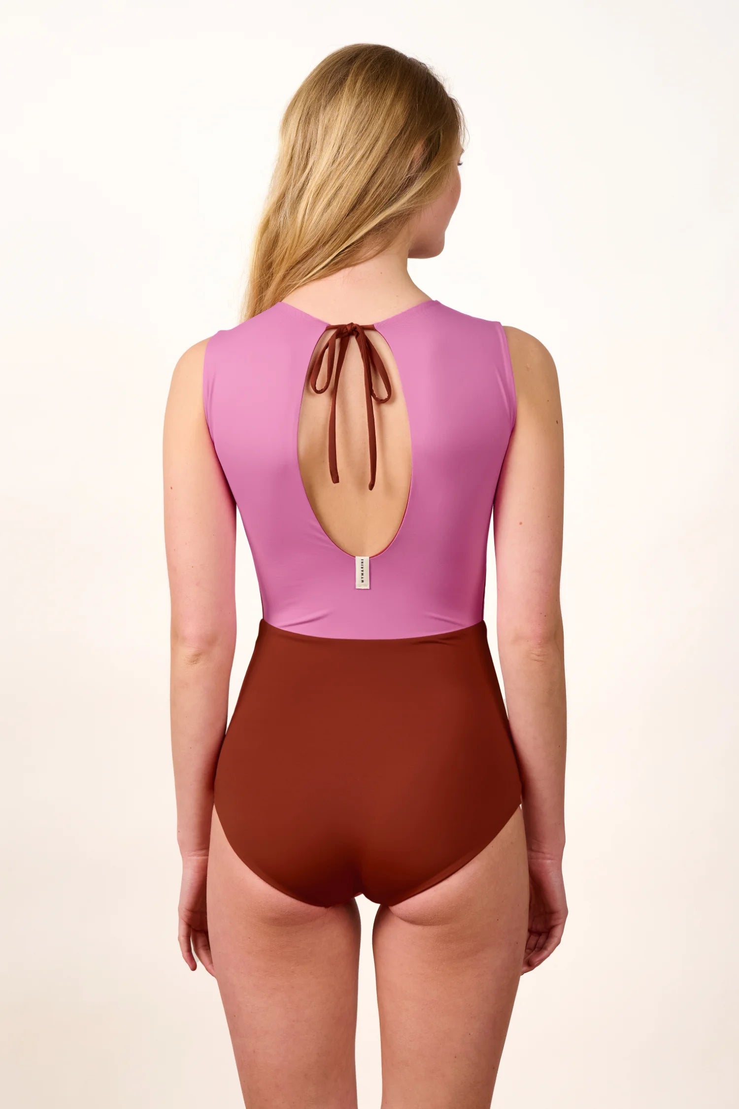 Frau in einem MYMARINI Badeanzug mit tiefem Rückenausschnitt und breiten Trägern in Rosa und Braun.#color_sienna-orchid