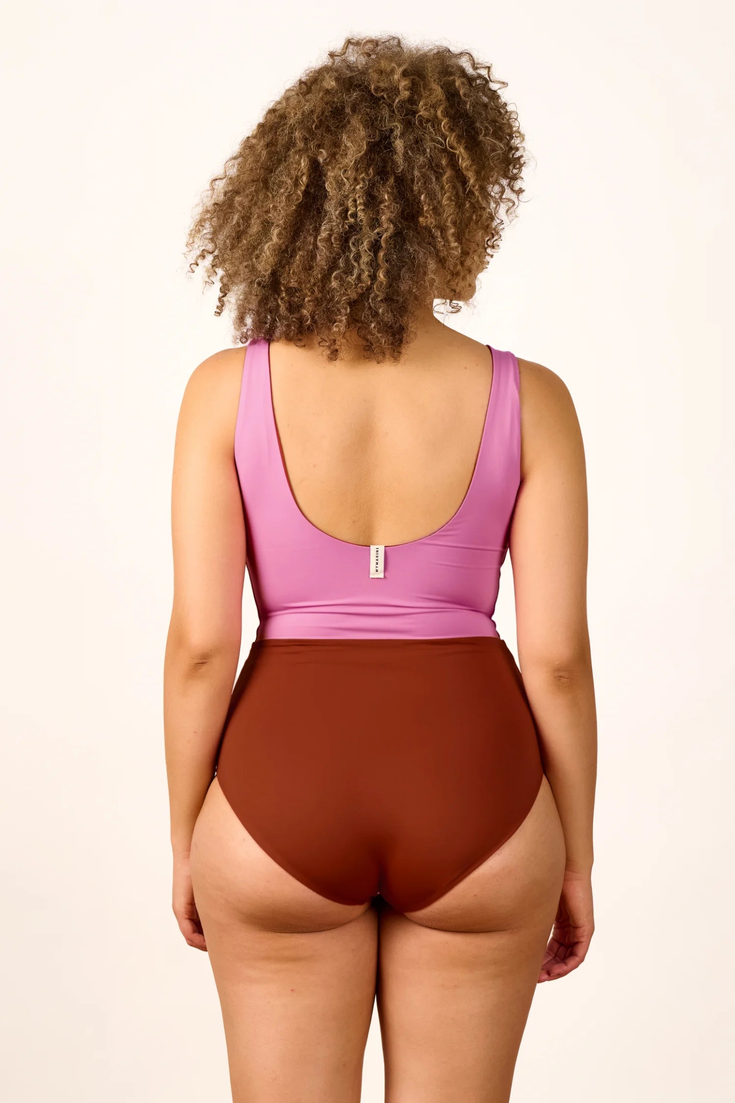 Person trägt einen MYMARINI Badeanzug mit tiefem Rückenausschnitt und hohem Beinausschnitt in Rosa und Braun.#color_sienna-orchid