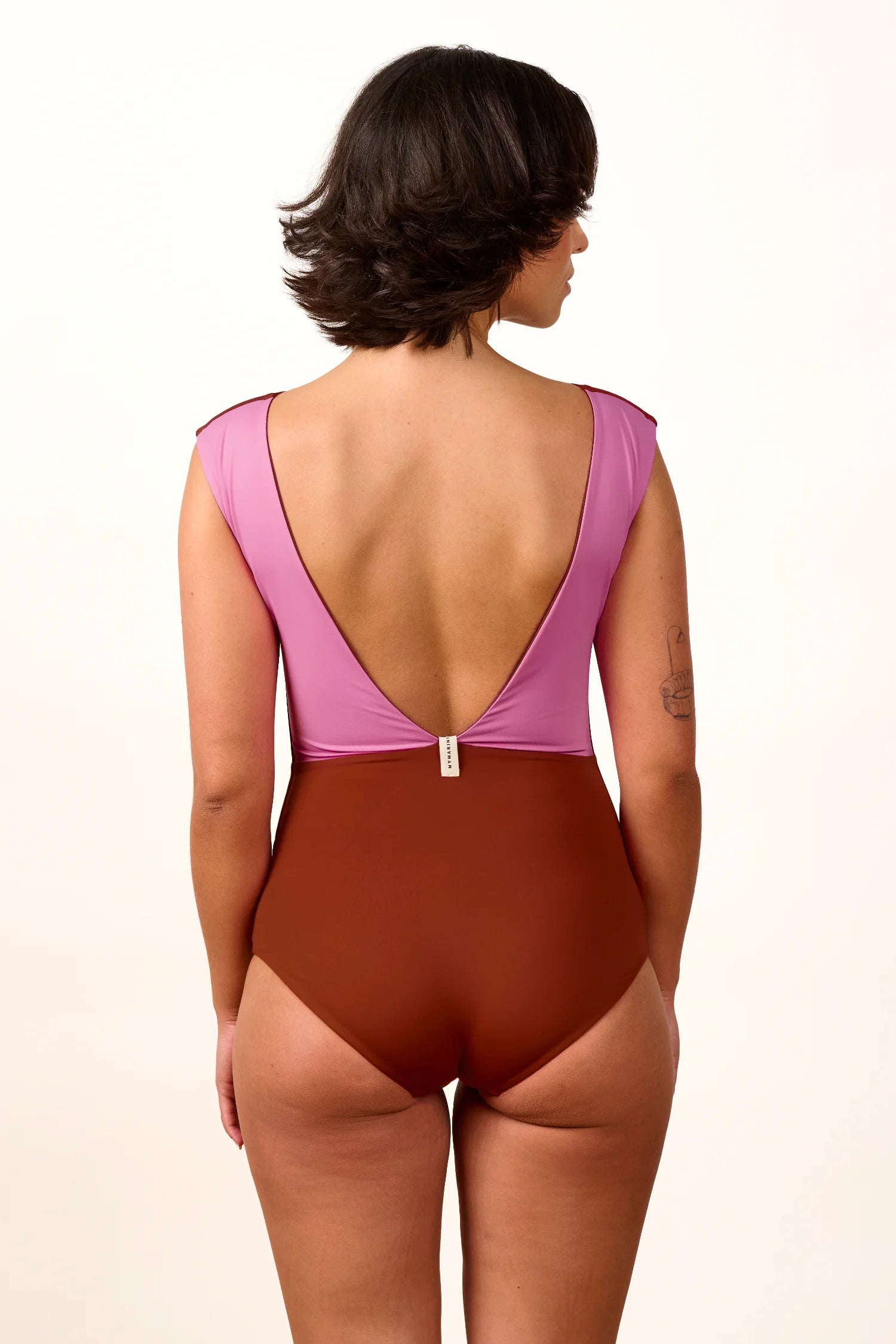 Frau in MYMARINI Badeanzug mit tiefem Rückenausschnitt und breiten Trägern in Rosa und Braun, von hinten gezeigt.#color_sienna-orchid