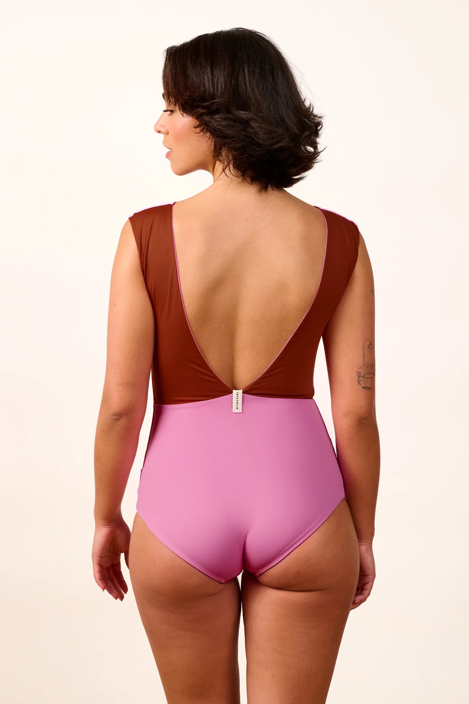 Frau im MYMARINI Badeanzug mit tiefem Rückenausschnitt und breiten Trägern in Braun und Rosa, von hinten gezeigt.#color_sienna-orchid