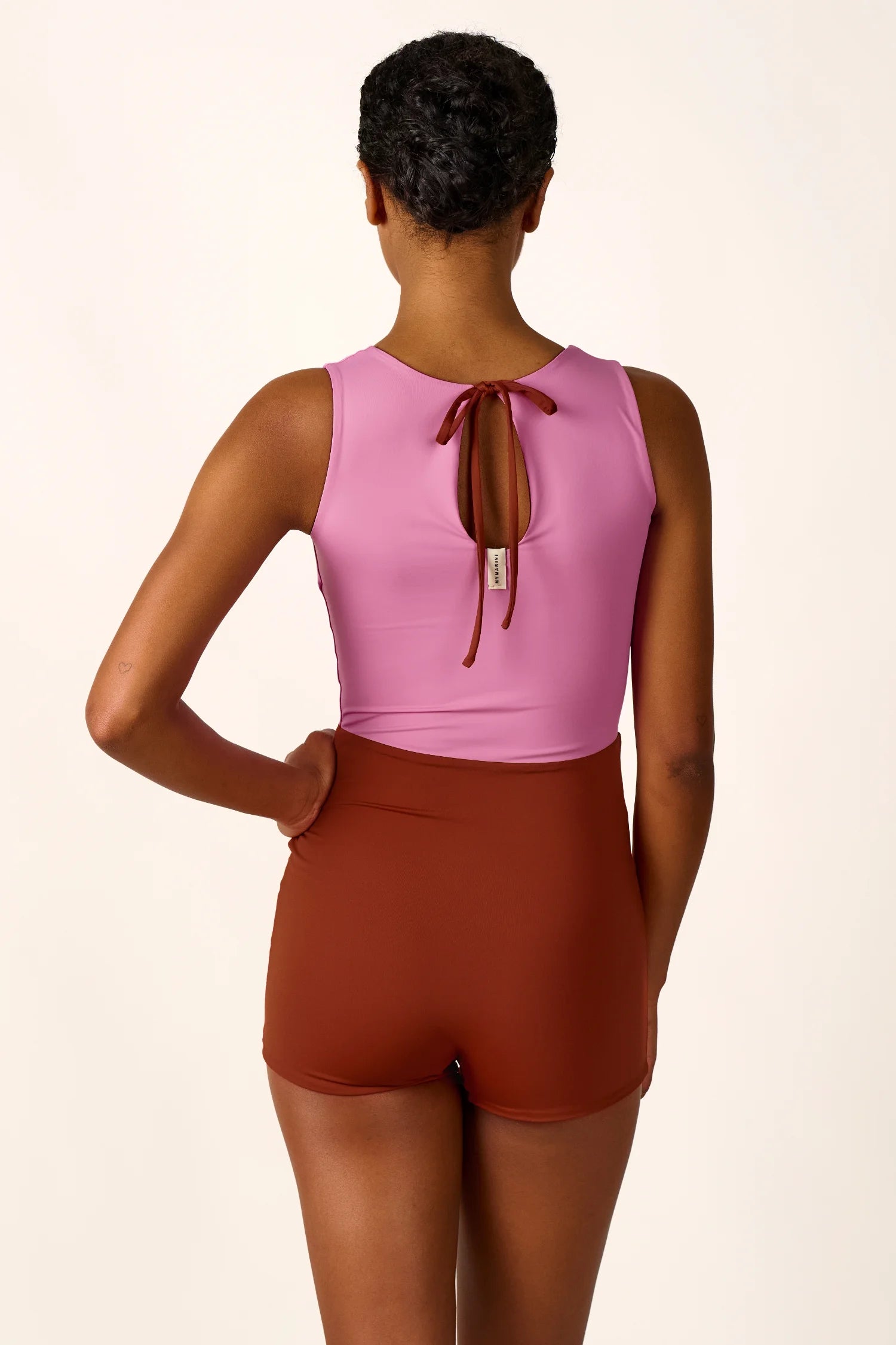 Person von hinten in einem MYMARINI Badeanzug mit hochgeschlossenem Schnitt und tiefem Rückenausschnitt in Rosa und Braun.#color_sienna-orchid