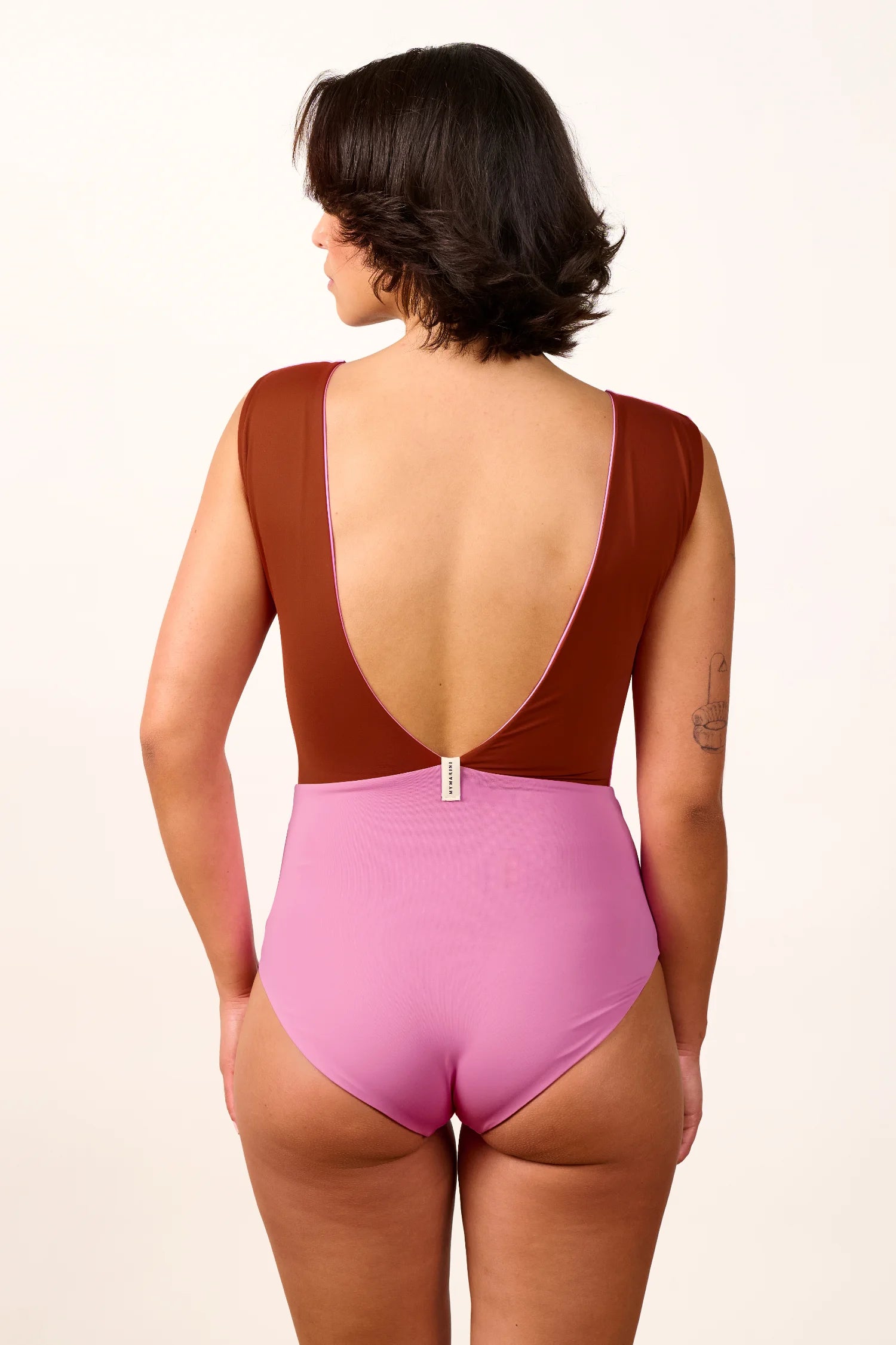 Frau trägt MYMARINI One-Piece mit tiefem Rückenausschnitt und breiten Trägern in Braun und Rosa.#color_sienna-orchid