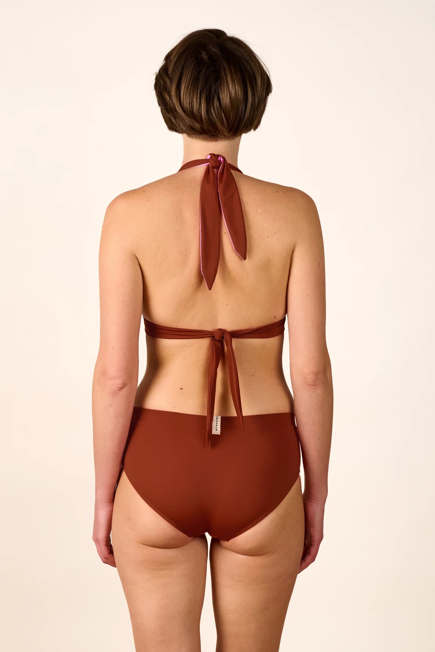 Rückansicht einer Person in einem MYMARINI Neckholder-Bikinitop und High-Waist-Bikinihose in Braun.#color_sienna-orchid