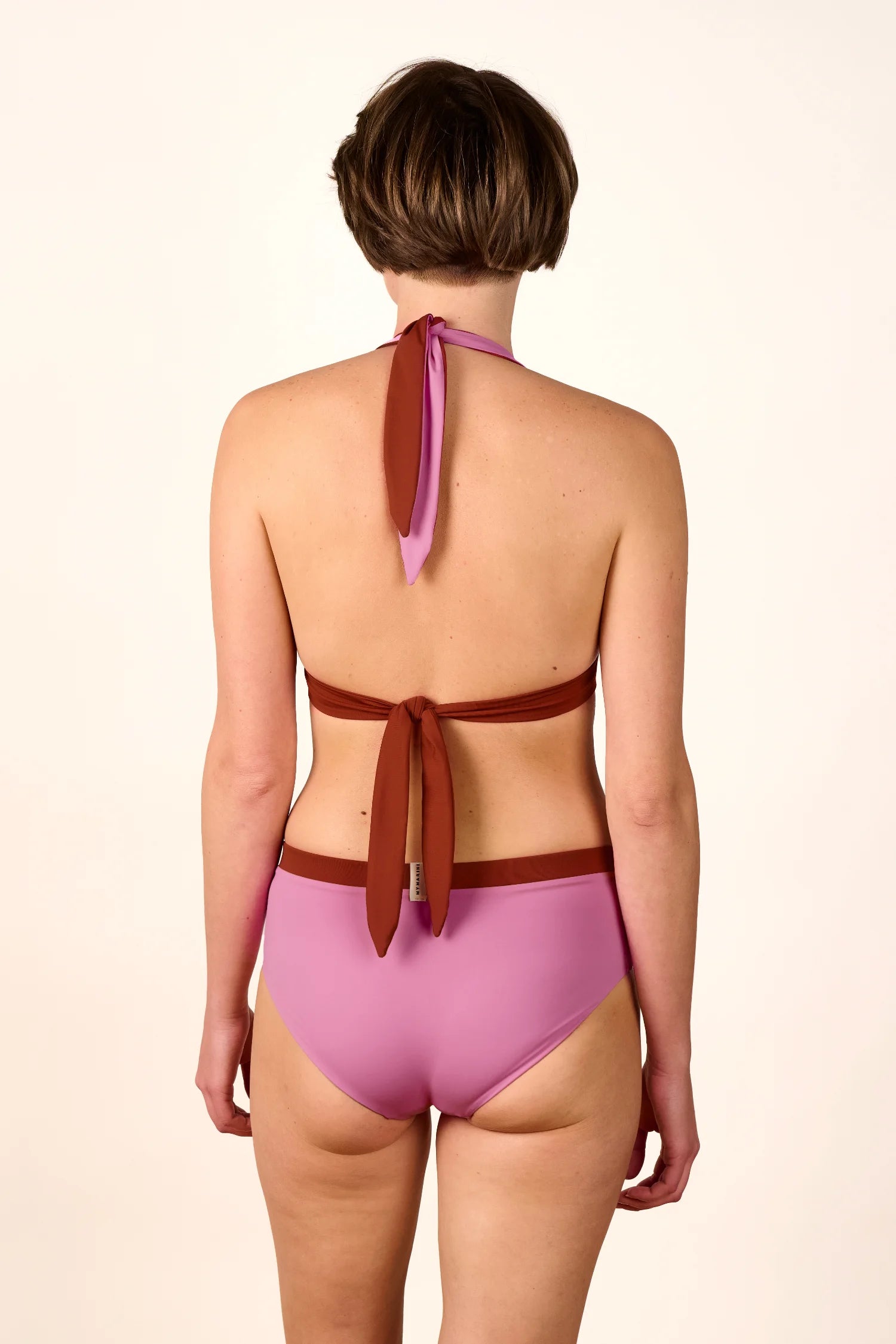 Rückansicht einer Person in einem MYMARINI Neckholder-Bikinitop und einer High-Waist-Bikinihose in Rosa und Braun.#color_sienna-orchid