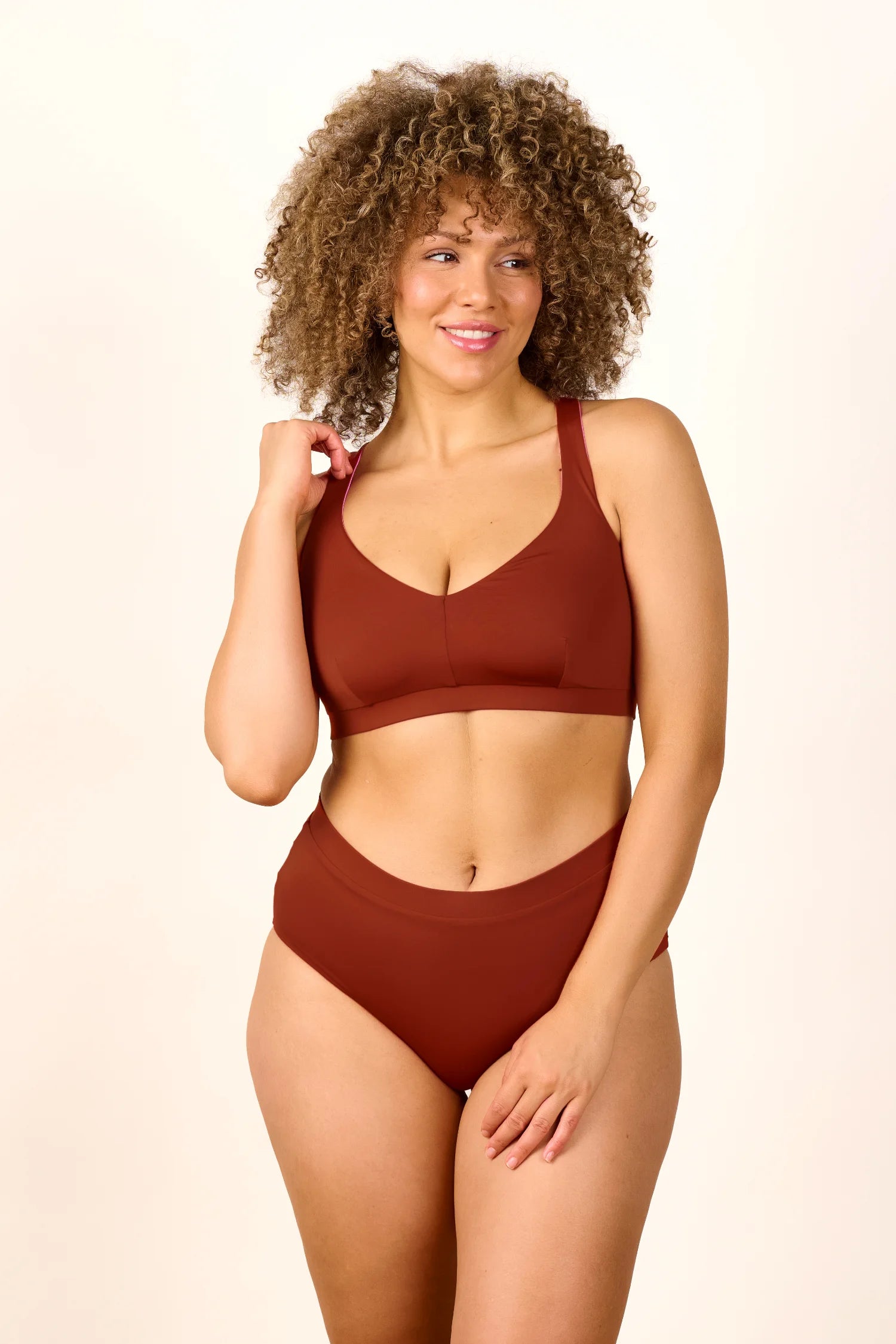 Frau trägt MYMARINI Bikini mit breiten Trägern und High-Waist-Schnitt in Braun, lächelnd vor hellem Hintergrund.#color_sienna-orchid