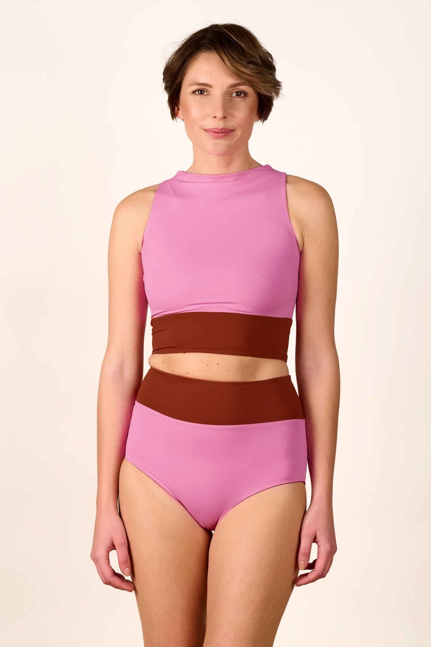 Person trägt MYMARINI Bikini mit hochgeschlossenem Top und High-Waist-Hose in Rosa und Braun, vor hellem Hintergrund.#color_sienna-orchid